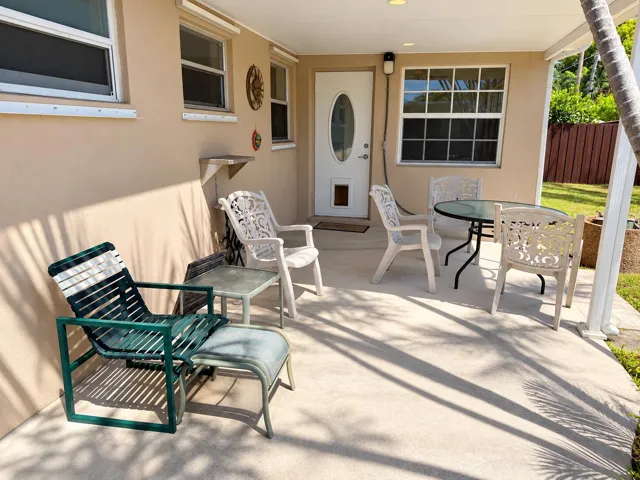 Covered patio with concrete flooring, accented by a white oval-paneled door and multiple windows