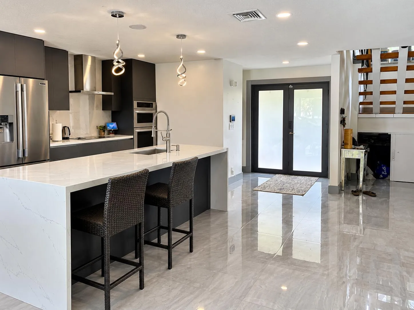 Kitchen featuring stainless steel appliances, dark flat-panel cabinetry, a large kitchen island with a light-toned countertop, and modern pendant lighting