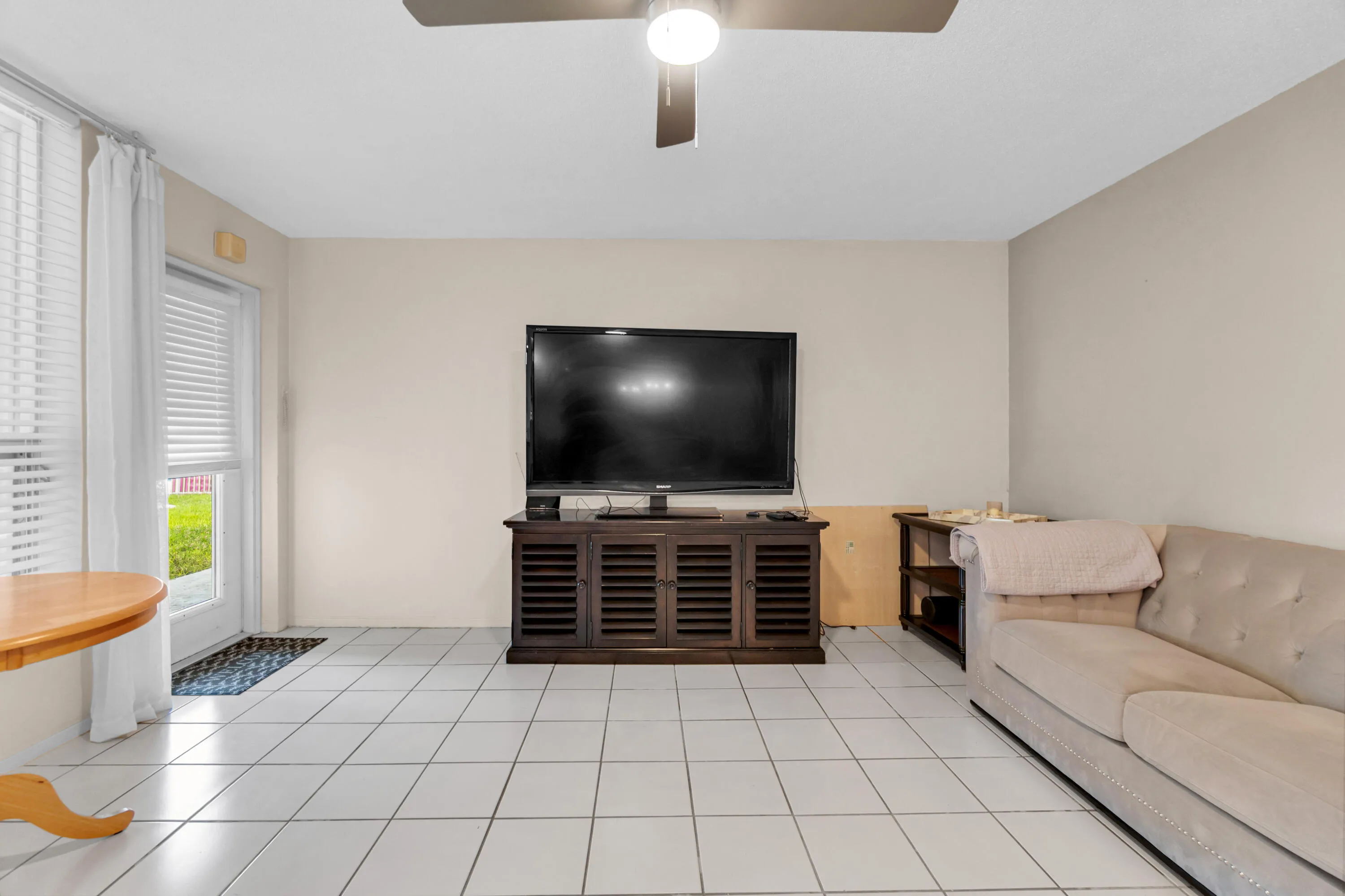 Light-toned square tile flooring, ceiling fan with integrated lighting, and a glass-paneled door with horizontal blinds
