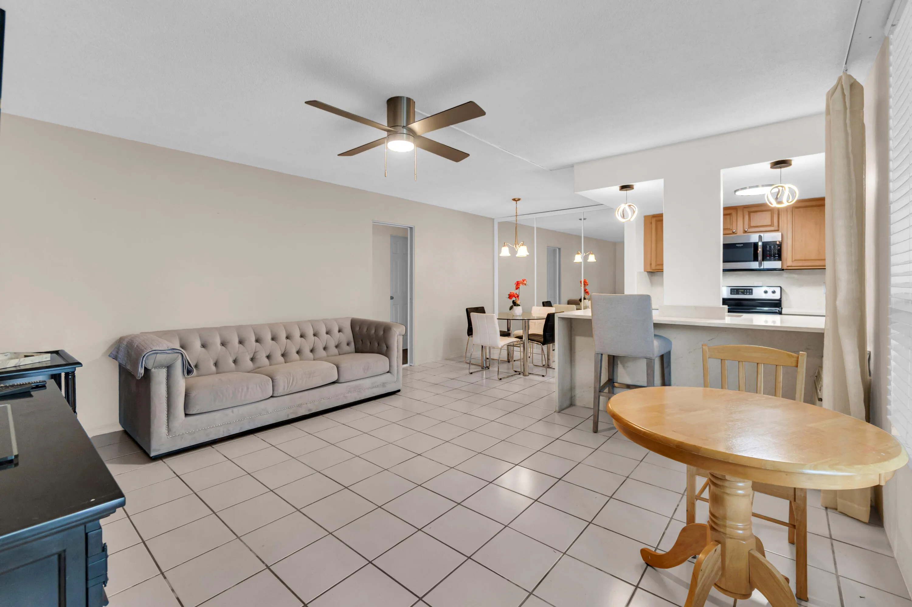 Open concept living area featuring tile flooring, ceiling fan, and recessed kitchen pass-through with pendant lighting