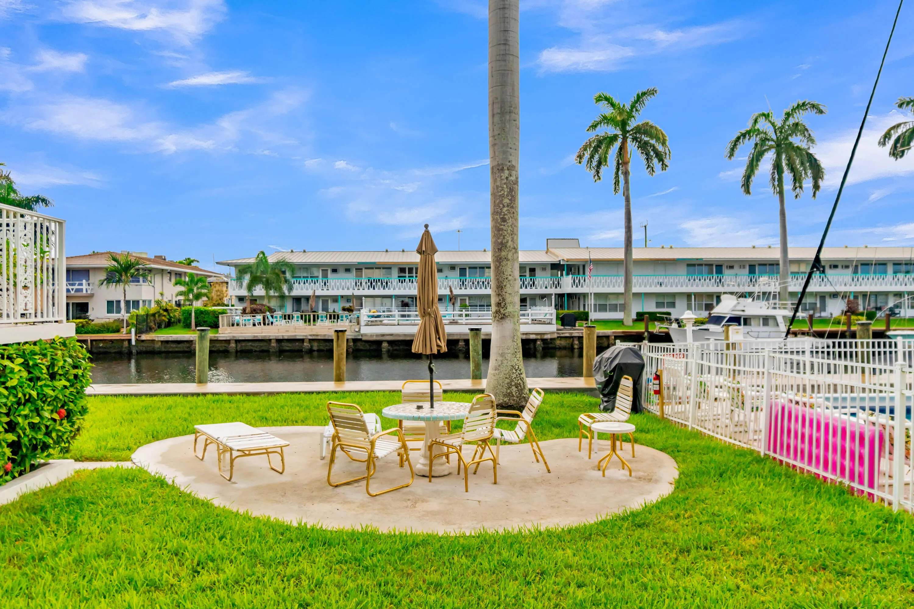 Manicured lawn with a concrete patio, white metal fencing, and water frontage