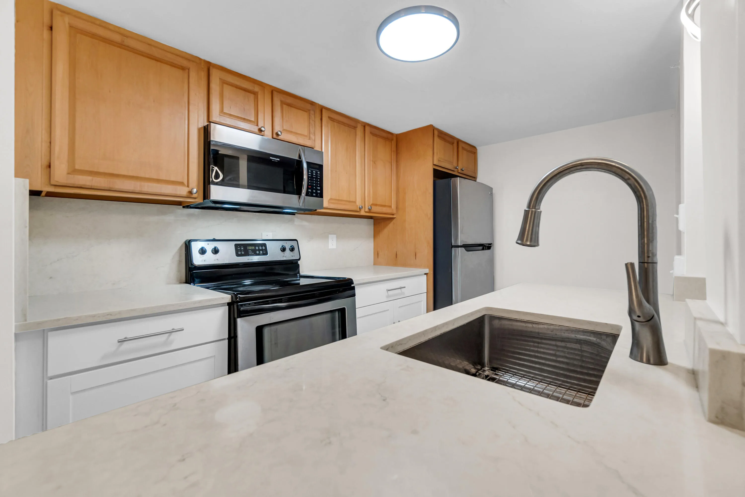 Kitchen featuring stainless steel appliances, light wood-finish cabinetry, light-toned countertops, and a single-basin sink with a gooseneck faucet