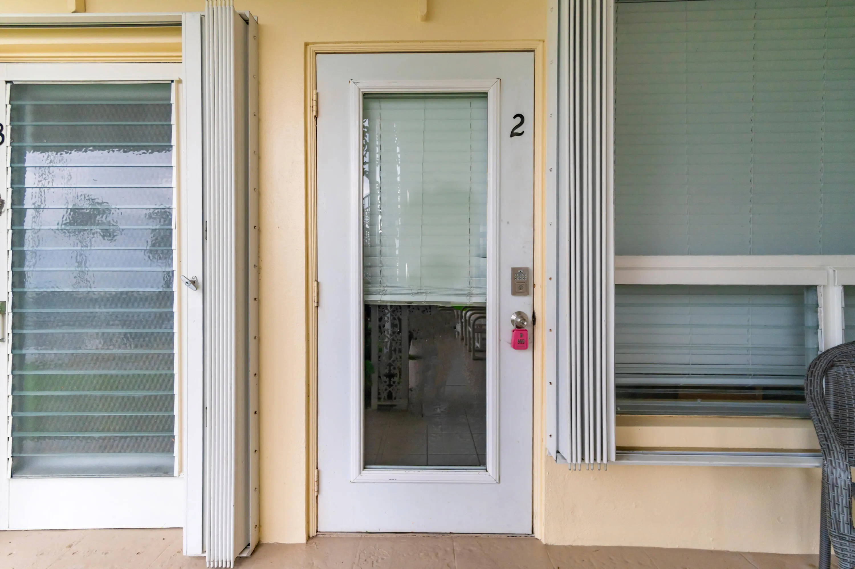 Entry door with glass panel, adjacent jalousie window, and exterior accordion shutters