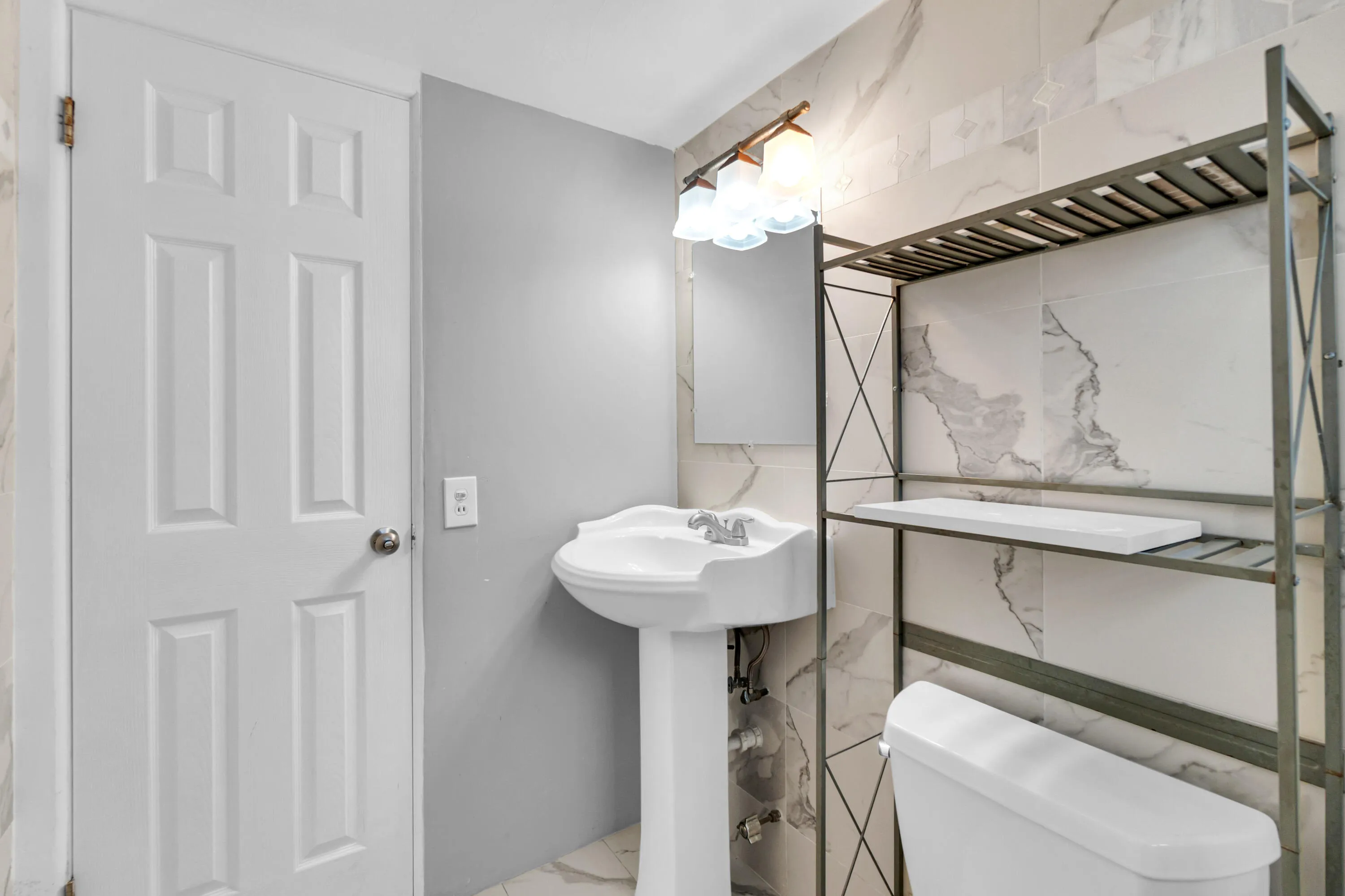 Pedestal sink with chrome faucet, wall-mounted light fixture, and white panel door