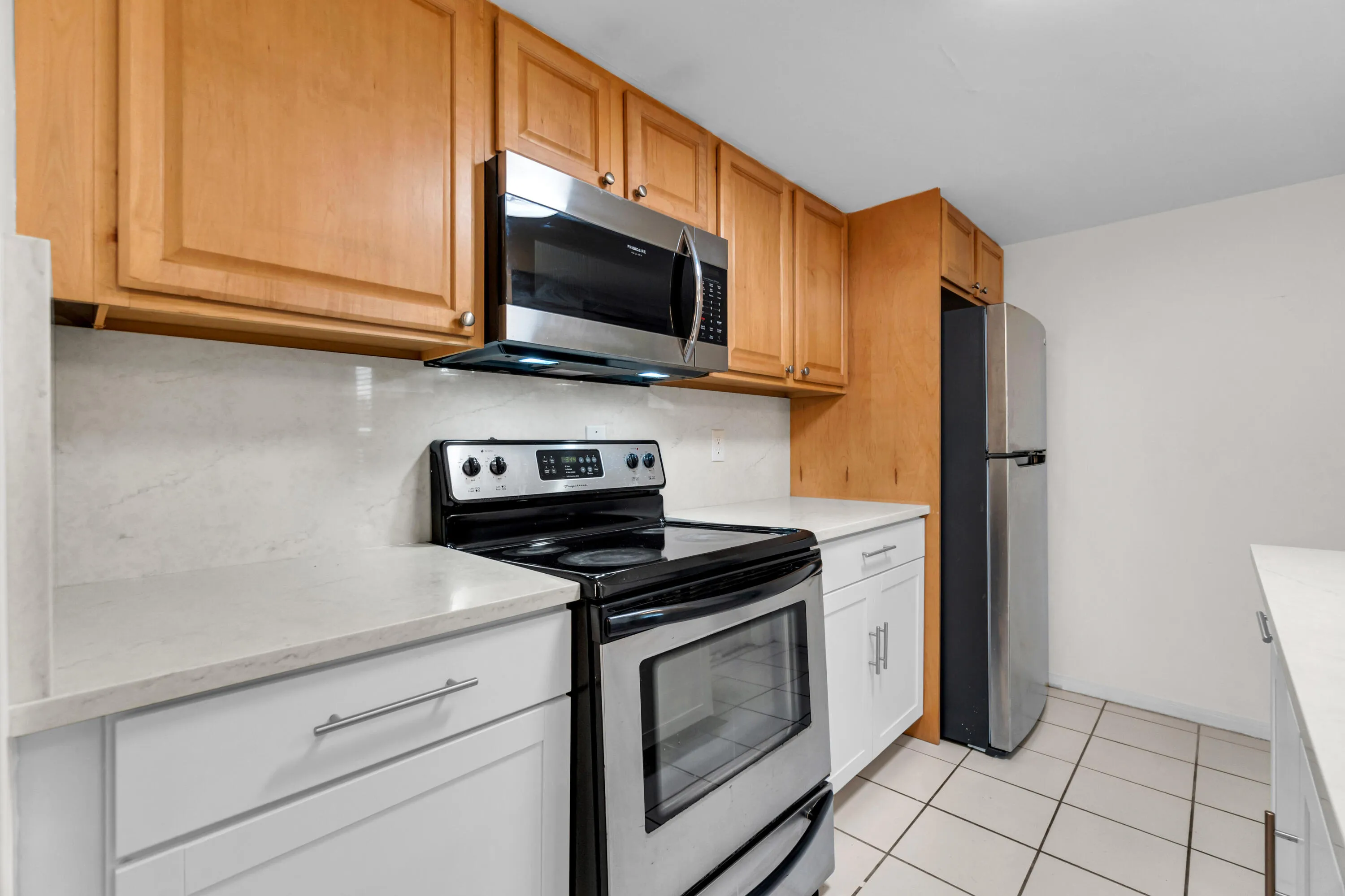Stainless steel appliances, light wood-finish cabinetry, white countertops, tile flooring, and a white backsplash