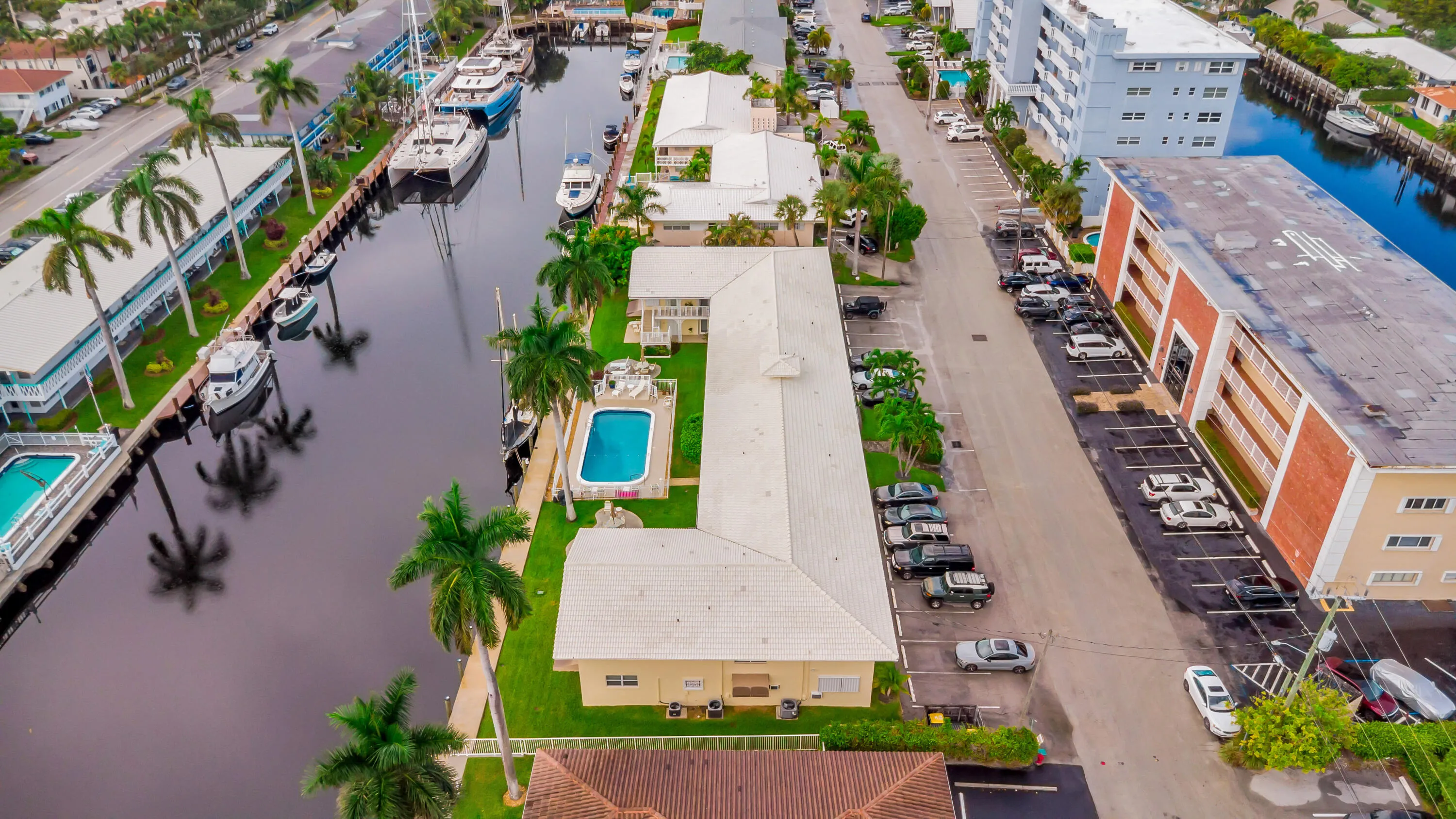 Waterfront property featuring a canal, mature palm trees, an outdoor swimming pool, and dedicated parking