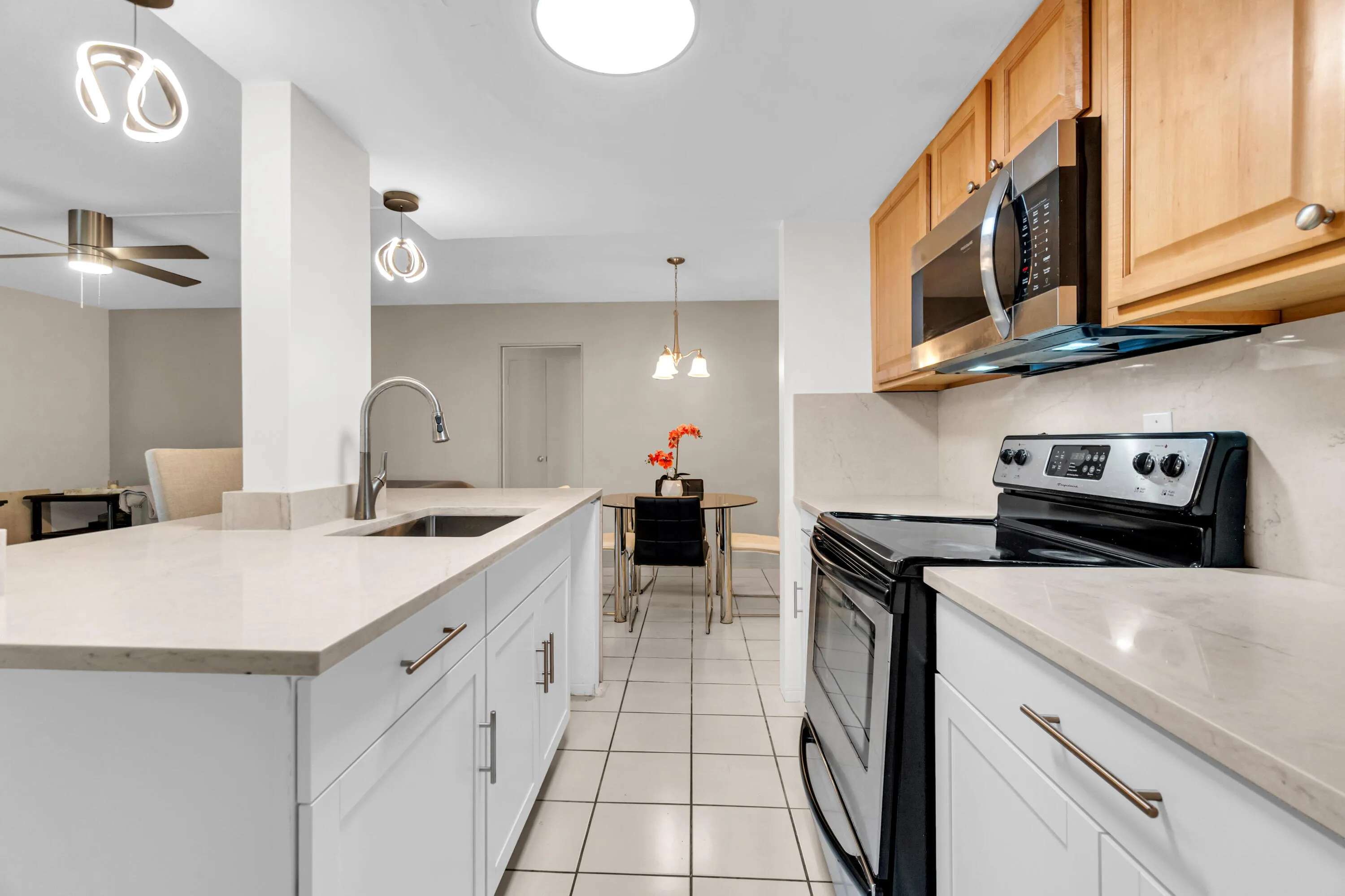 Kitchen featuring an island with an undermount sink, white cabinetry, light-toned countertops, and stainless steel appliances