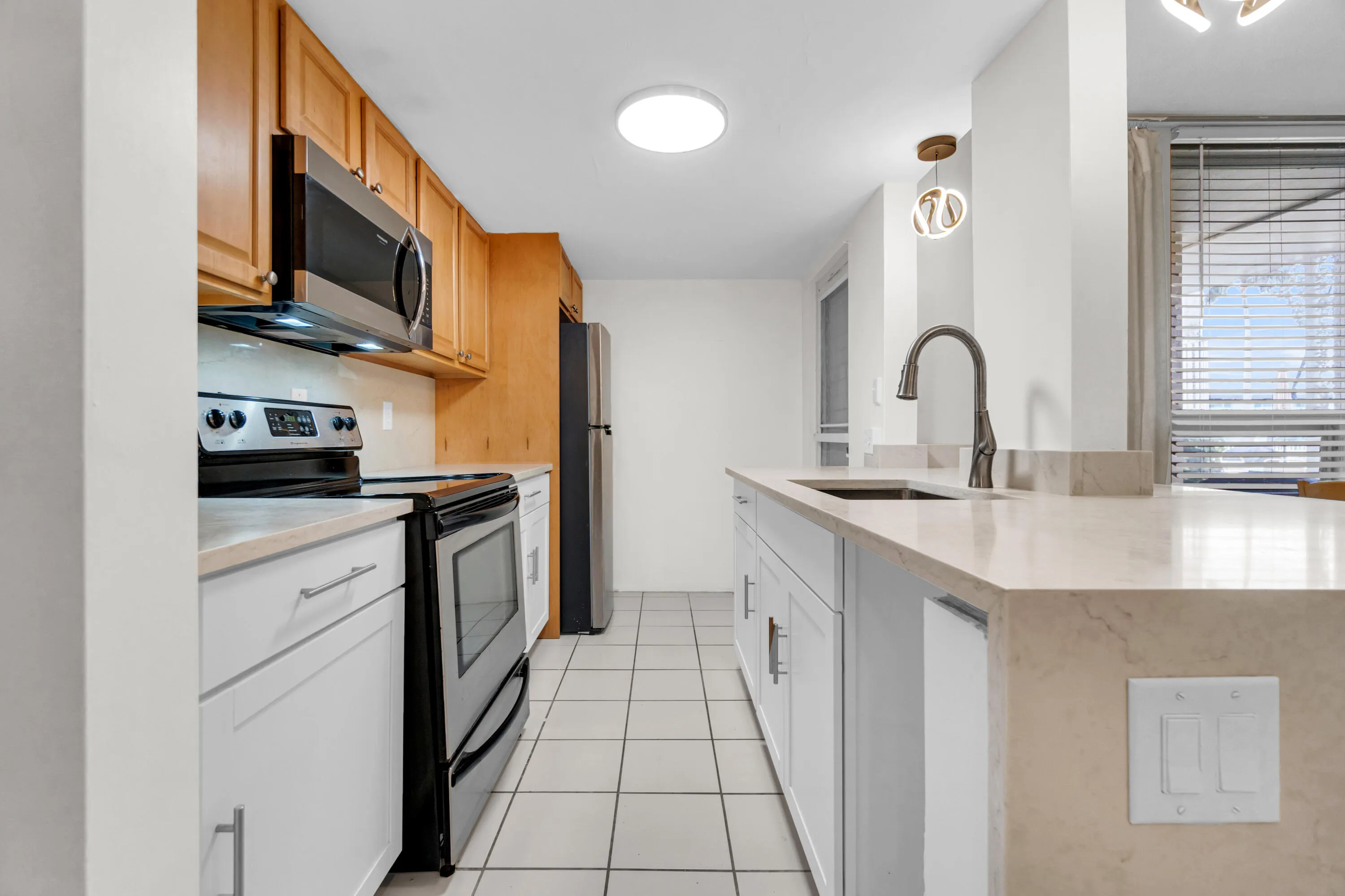 Kitchen featuring stainless steel appliances, light wood-finish cabinetry, light-toned countertops, and tile flooring