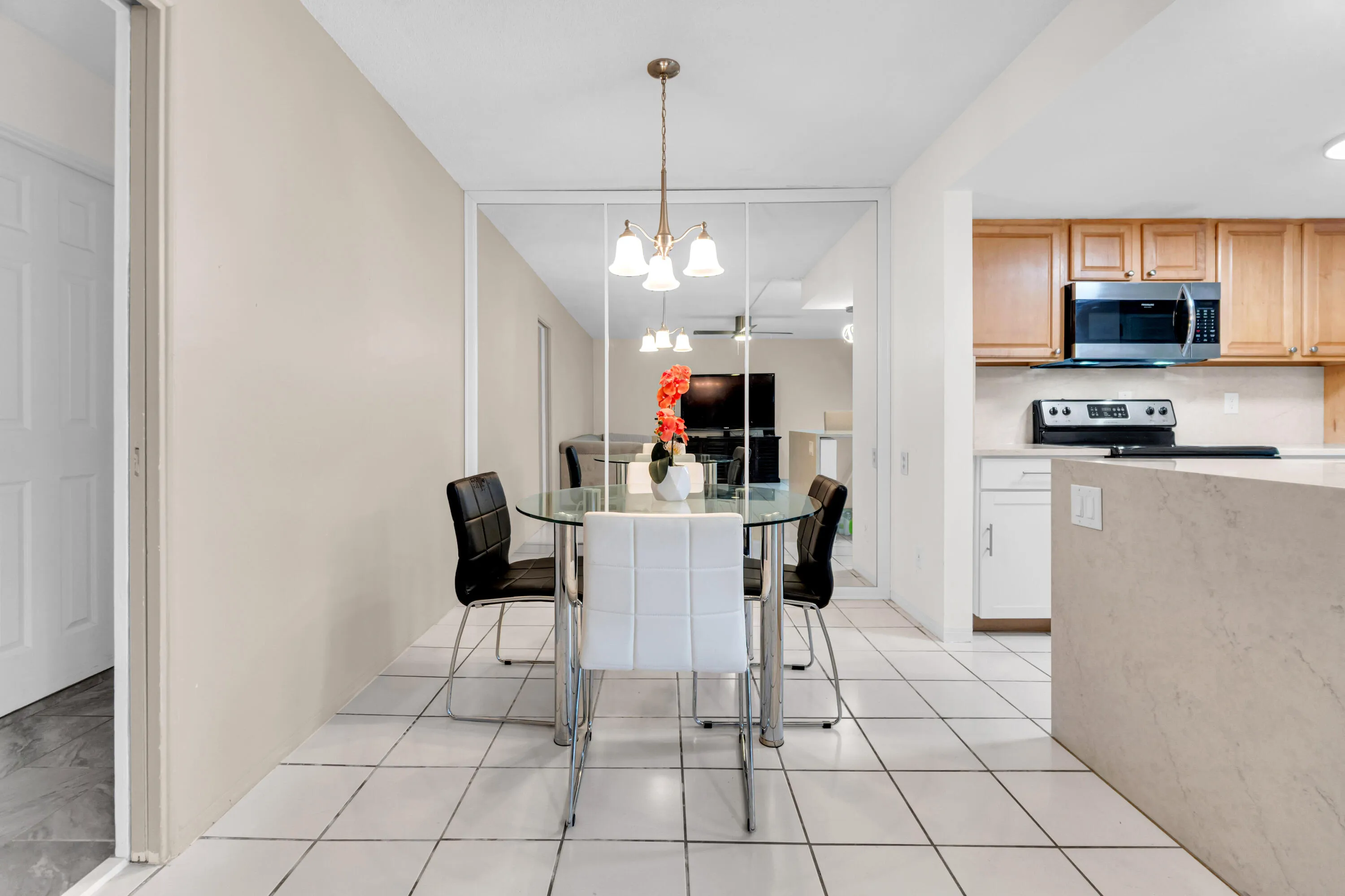 Tiled flooring with a warm-toned wall finish, mirrored wall panels, and a kitchen featuring wood-finish cabinetry and a built-in microwave