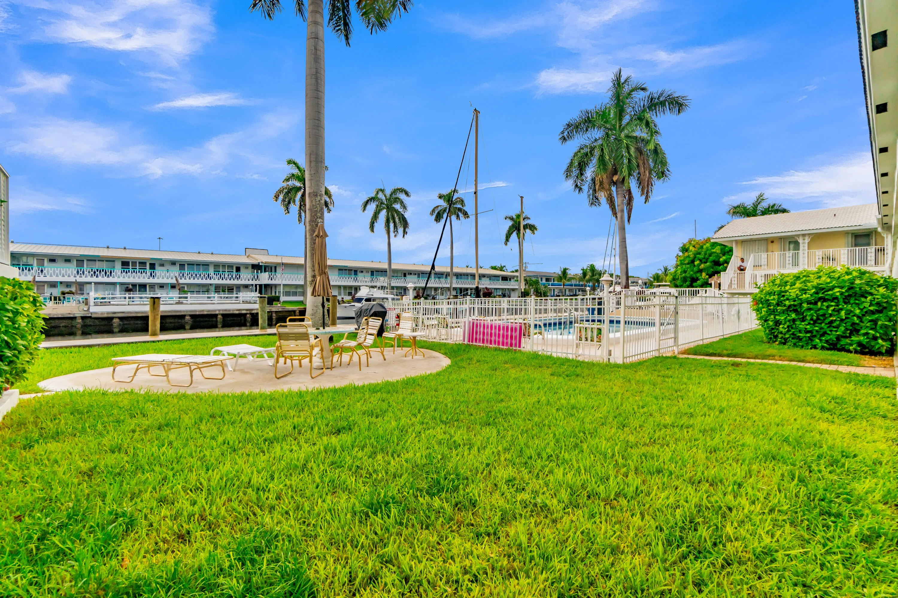 Expansive grassy area with a concrete patio, adjacent to a fenced swimming pool