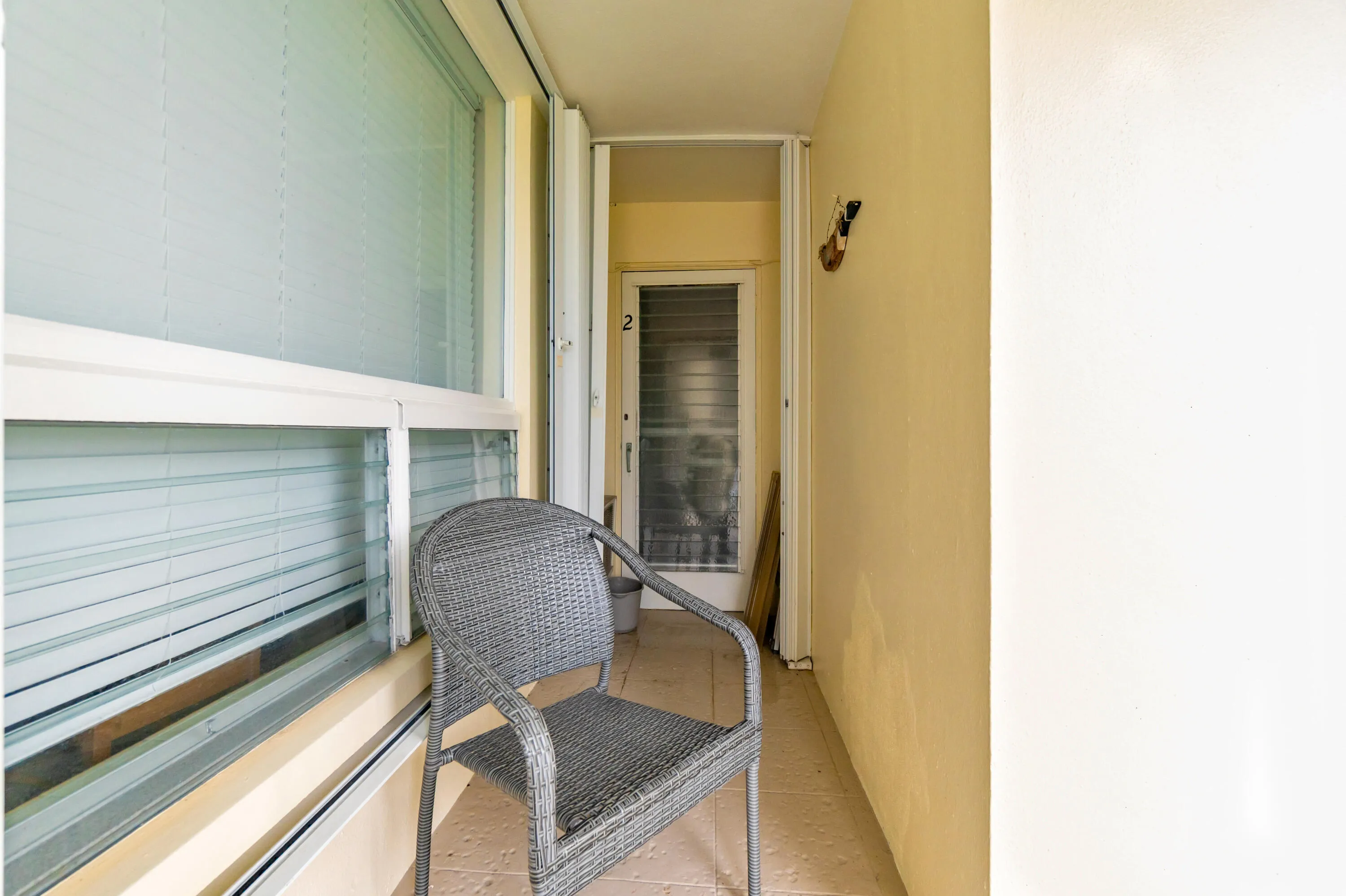 Enclosed balcony featuring large windows with blinds and a textured floor