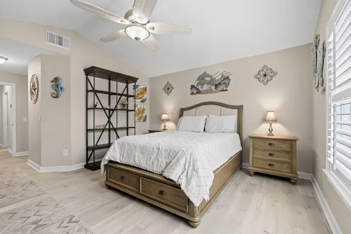 Angled ceiling, ceiling fan with integrated lighting, wood-finish flooring, and white plantation shutters