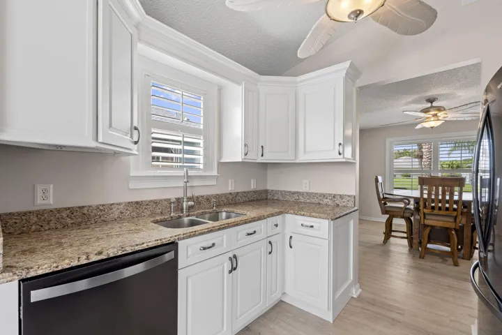 White cabinetry with dark hardware, stone-finish countertops, and a double basin sink