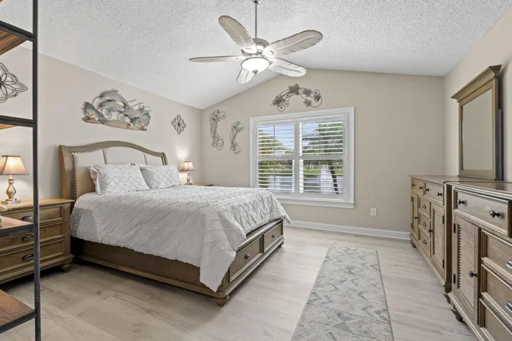 Vaulted ceiling with a ceiling fan, recessed window with plantation shutters, light wood-finish flooring, and light neutral wall tones