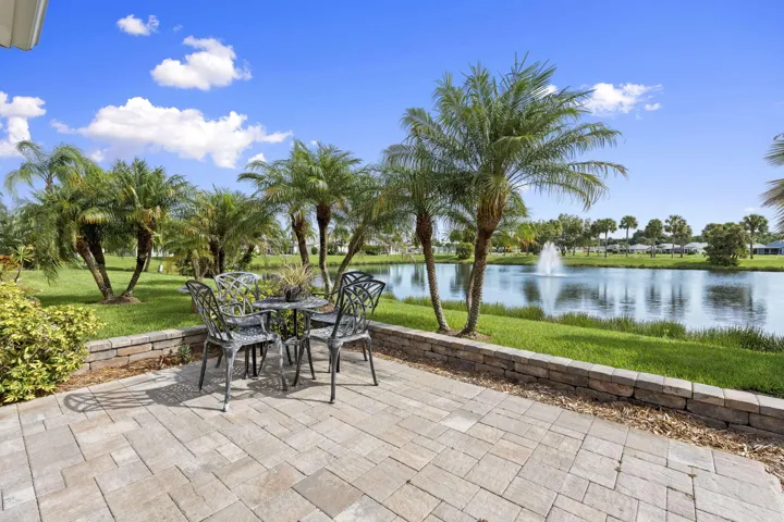 Paver patio with stone retaining wall, overlooking a body of water with a fountain, surrounded by mature palm trees and manicured lawn