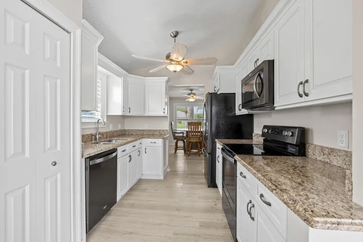 Galley kitchen featuring white cabinetry, light-toned countertops, and black appliances