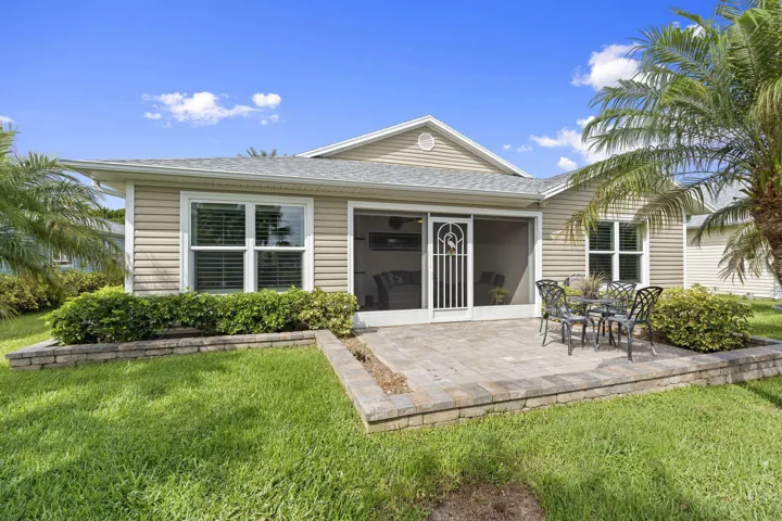 Vinyl siding exterior with a screened lanai, an elevated paver patio, and mature palm trees