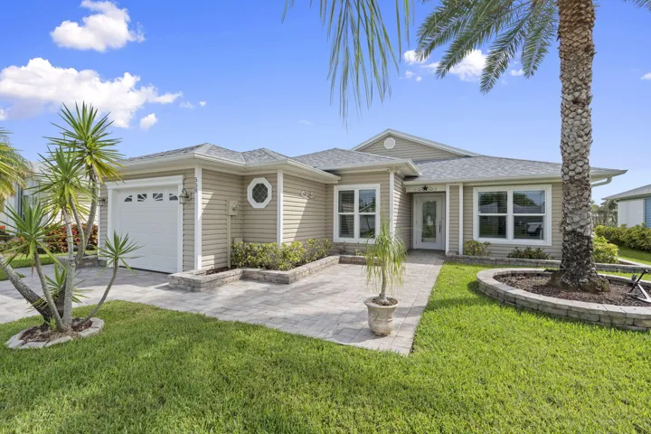 Single-story home featuring a light-colored siding exterior, an attached garage, a paved driveway, and a front walkway leading to the entry