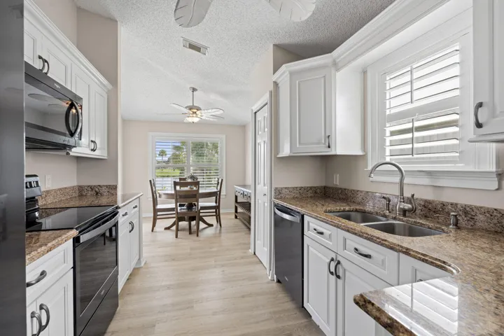 Kitchen featuring white cabinetry, stone countertops, black appliances, and wood-finish flooring