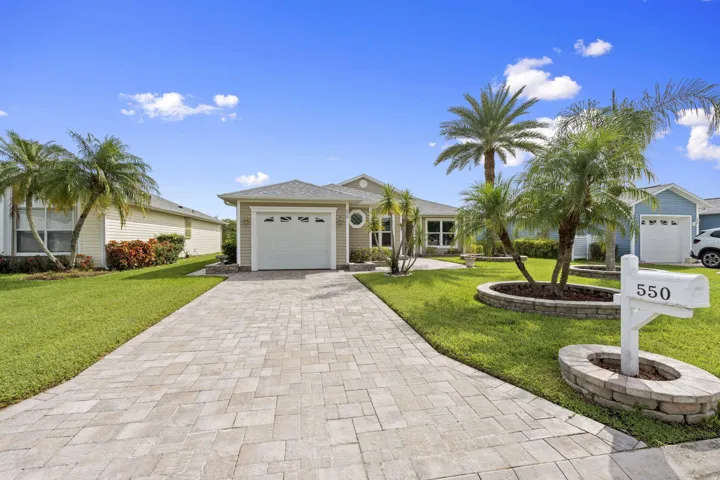 Single-story residence with siding exterior, attached garage, paver driveway, and mature landscaping with palm trees