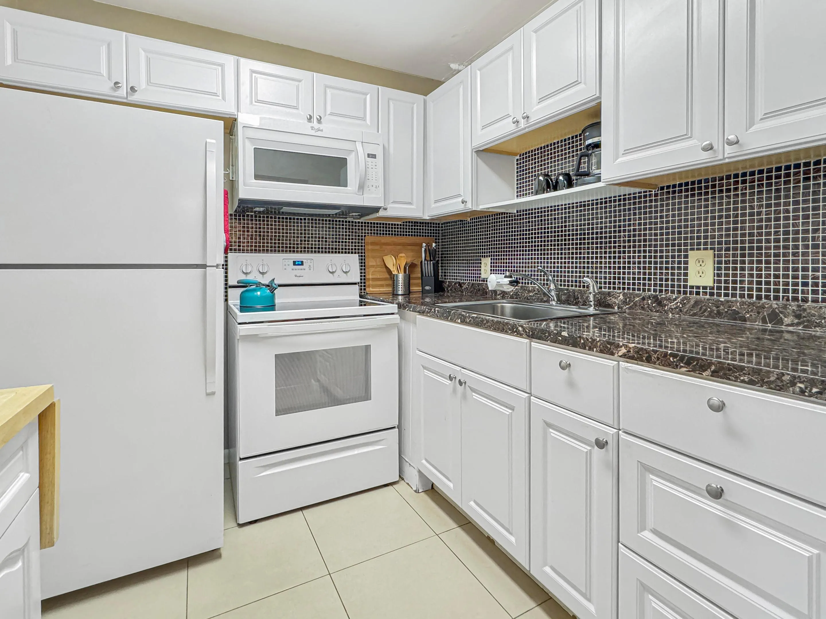 White cabinetry with brushed nickel hardware, dark mosaic tile backsplash, solid surface countertops, and white appliances