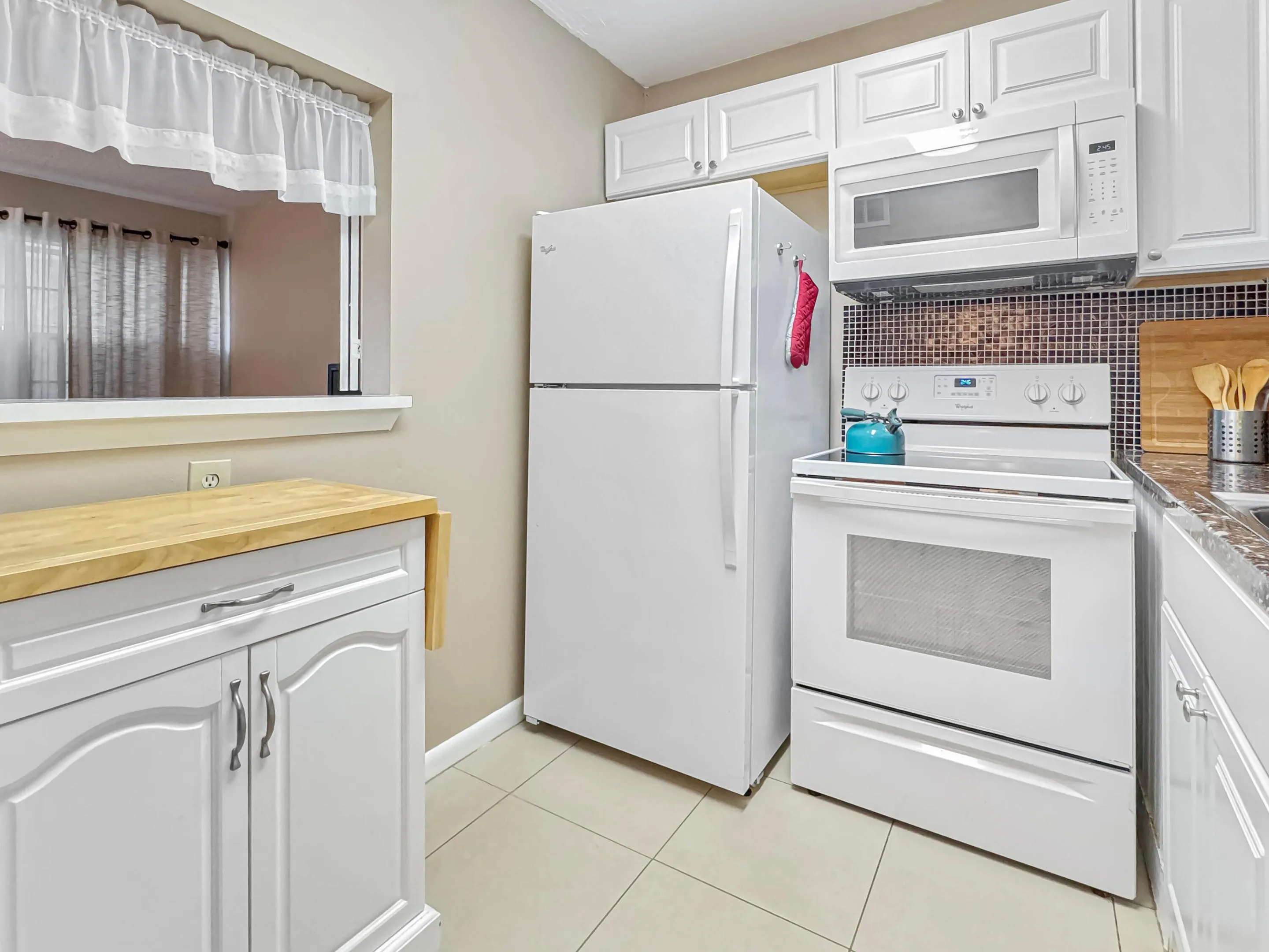 Kitchen featuring white cabinetry, tile flooring, mosaic tile backsplash, and a pass-through window
