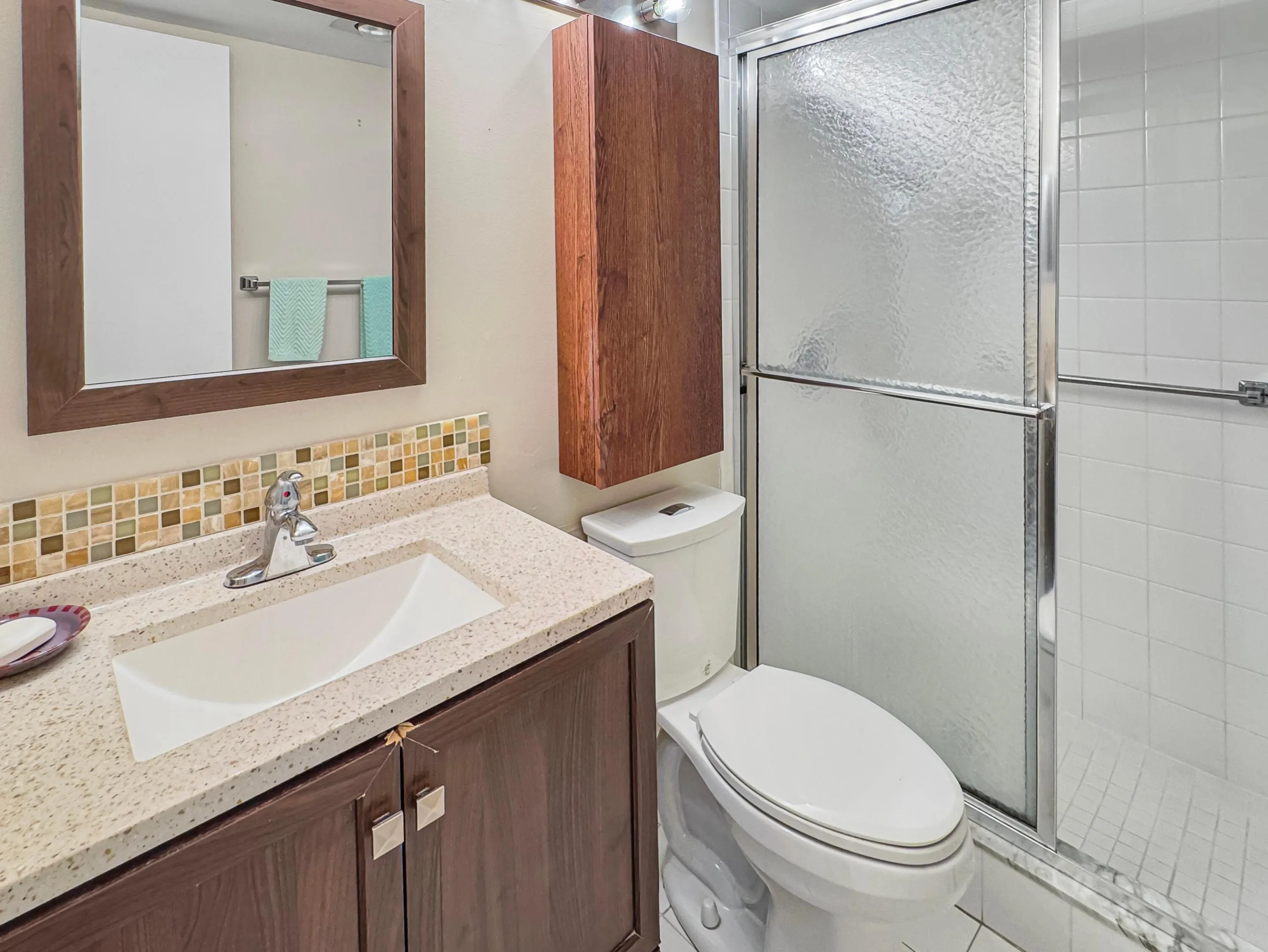 Bathroom featuring a vanity with an integrated sink, mosaic tile backsplash, wood-finish cabinetry, and a shower with sliding glass doors