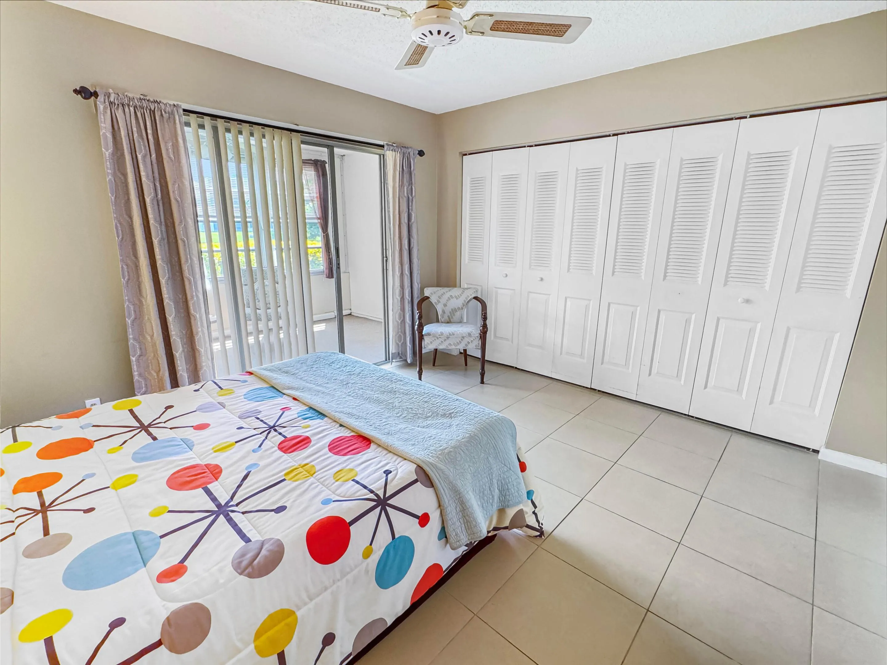 Tile flooring, sliding glass door, overhead ceiling fan, and louvered bi-fold closet doors