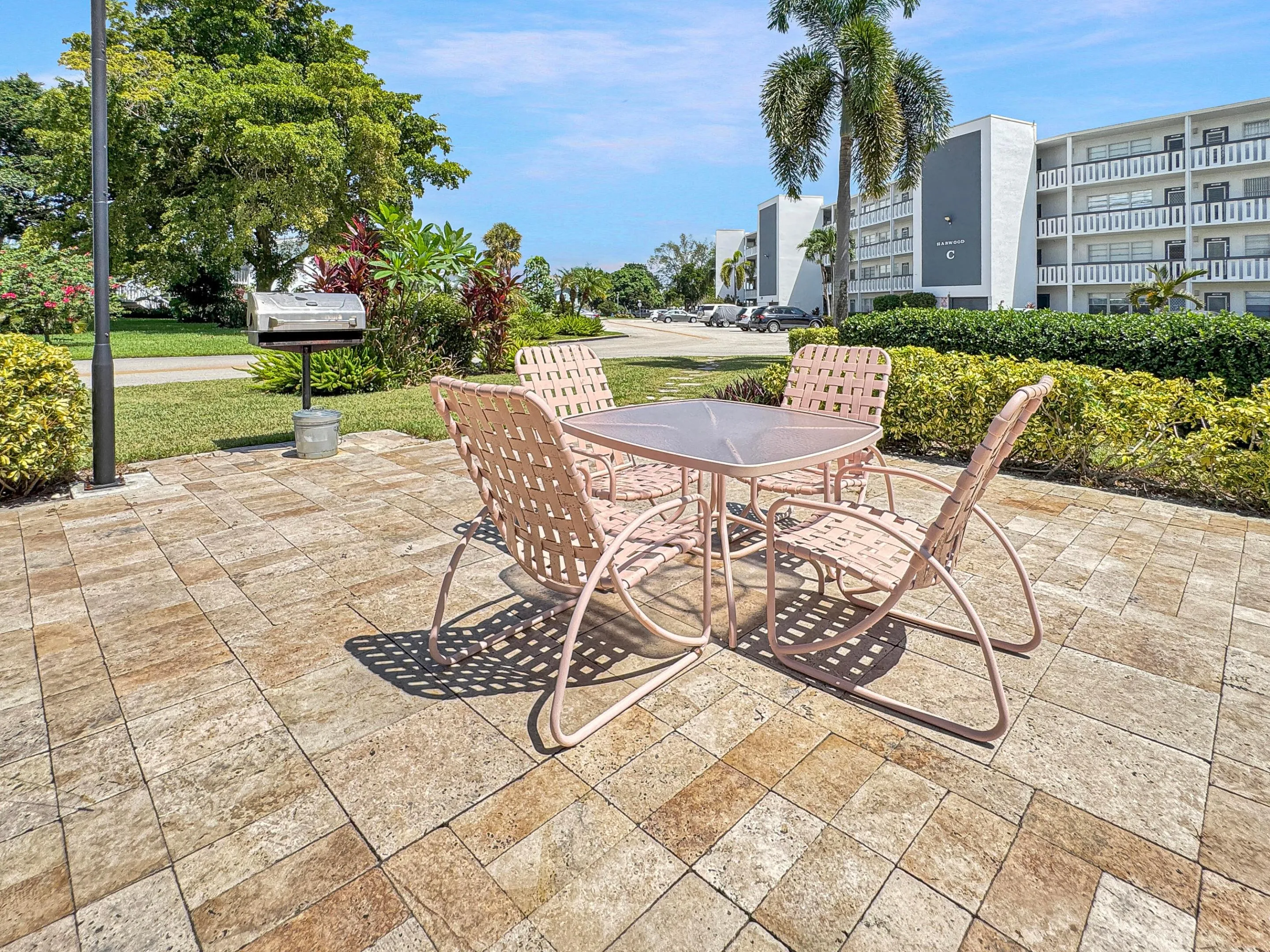 Paver patio surface, integrated outdoor grill, mature landscaping, well-maintained lawn, and multi-story building exterior