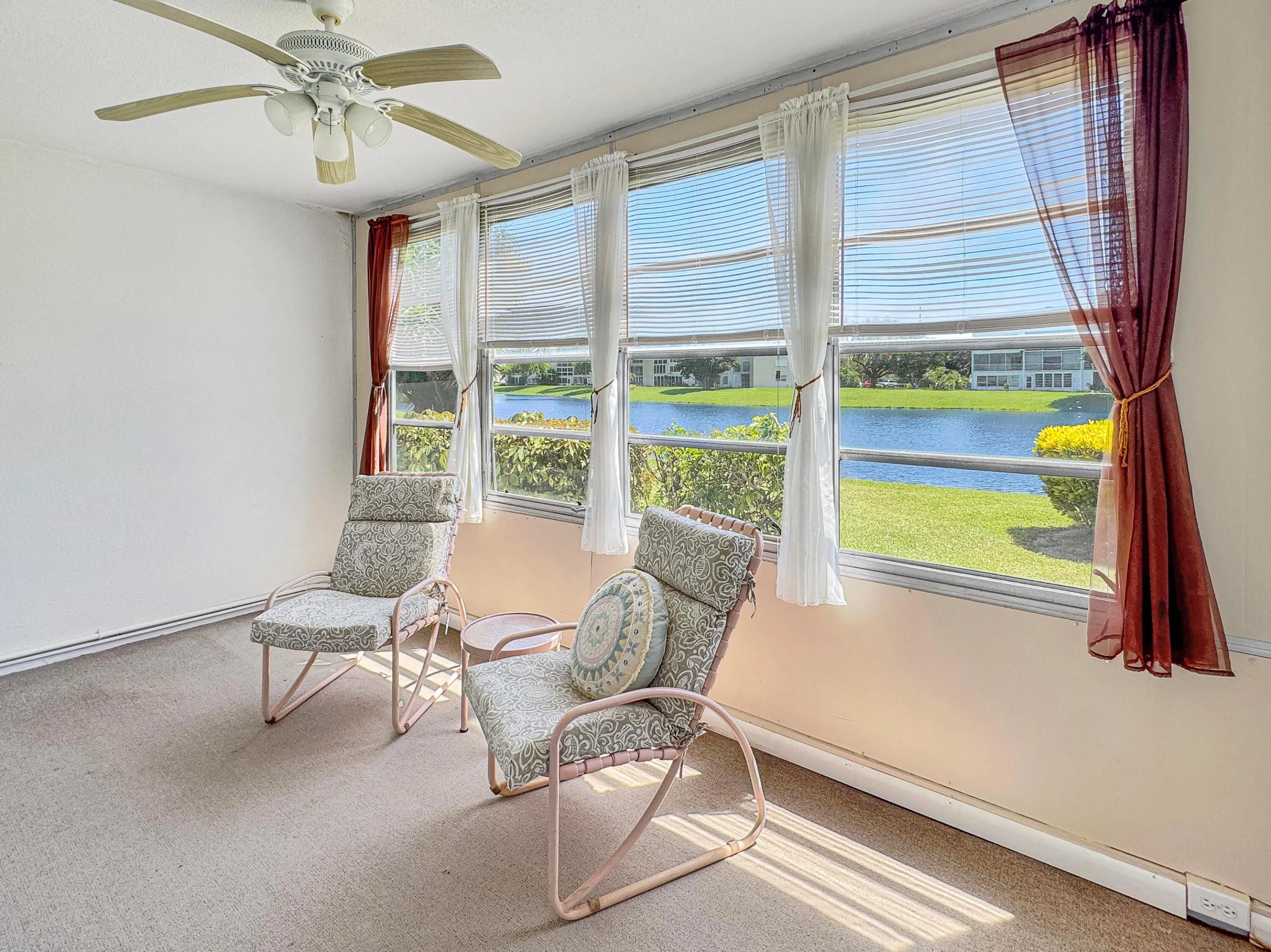 Expansive windows showcasing water frontage, ceiling fan with integrated lighting, and neutral wall tones