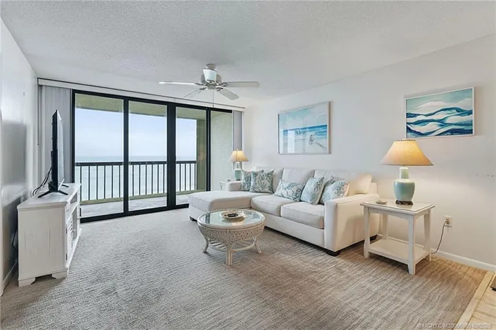 Oceanfront living room with floor-to-ceiling sliding glass doors opening to the balcony and direct Atlantic Ocean views. Virtually staged.