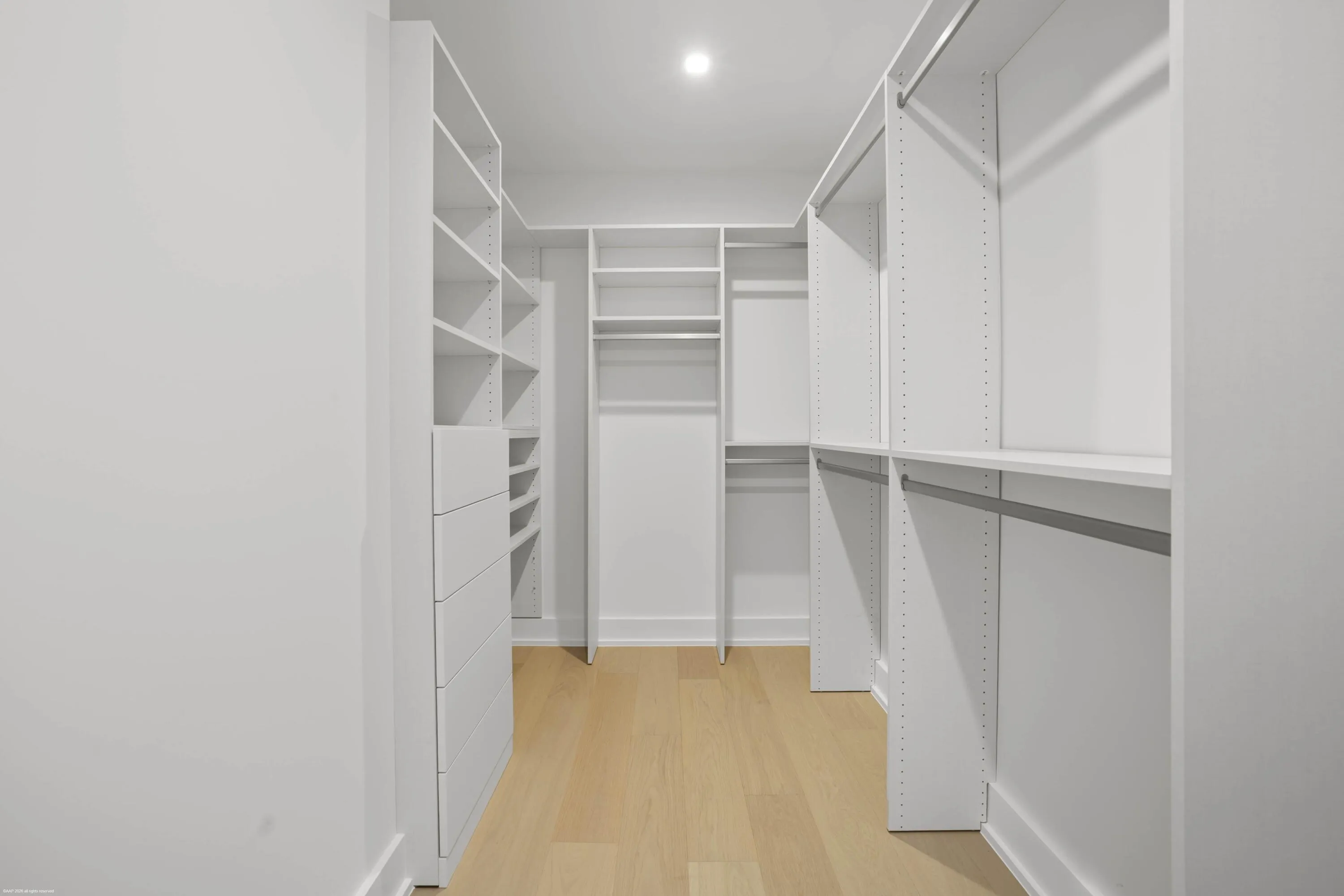 Walk-in closet featuring light wood-finish flooring, recessed lighting, white built-in shelving, integrated drawers, and hanging rods