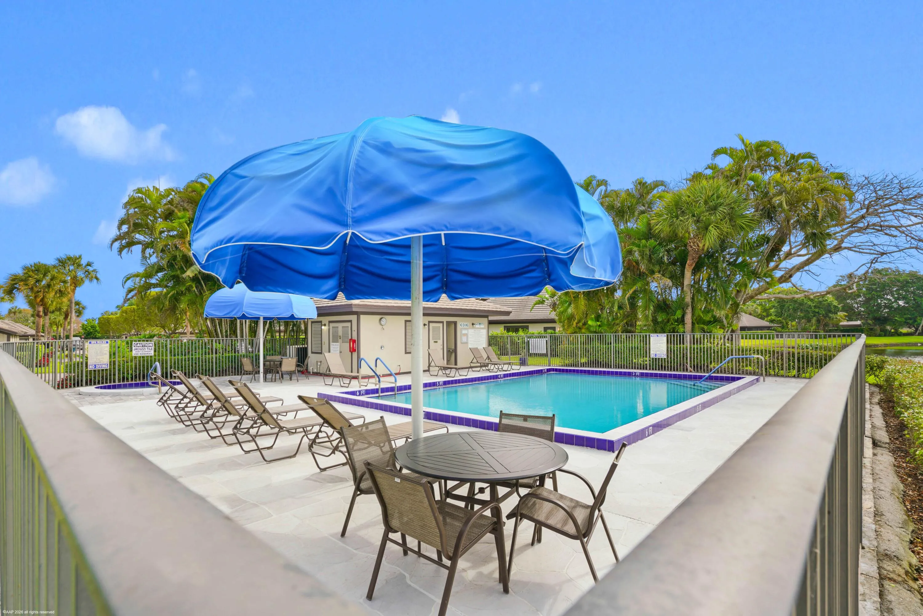 Community swimming pool with surrounding lounge seating, a shaded dining area, and mature tropical landscaping