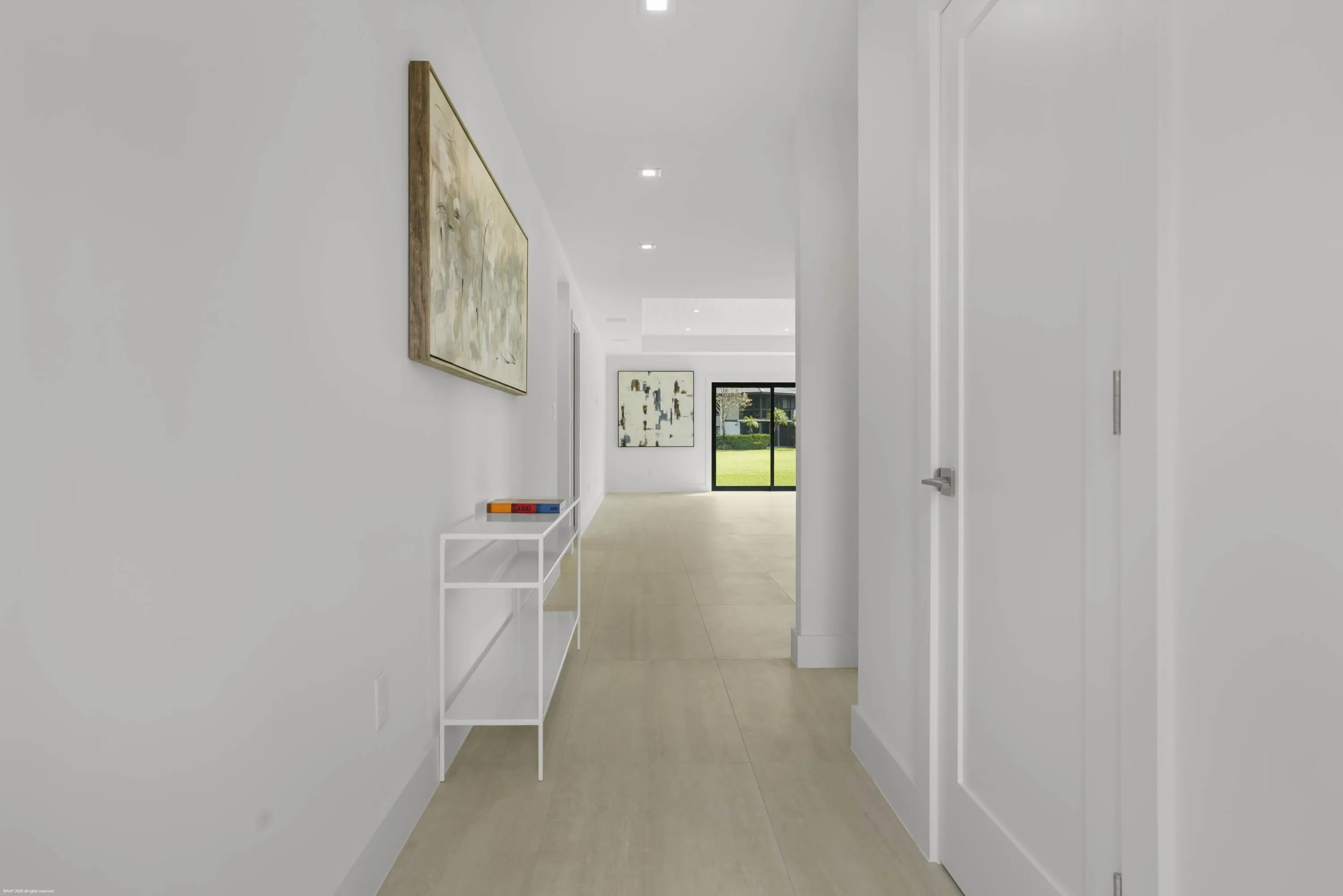 Recessed lighting illuminates a long hallway with light-toned flooring