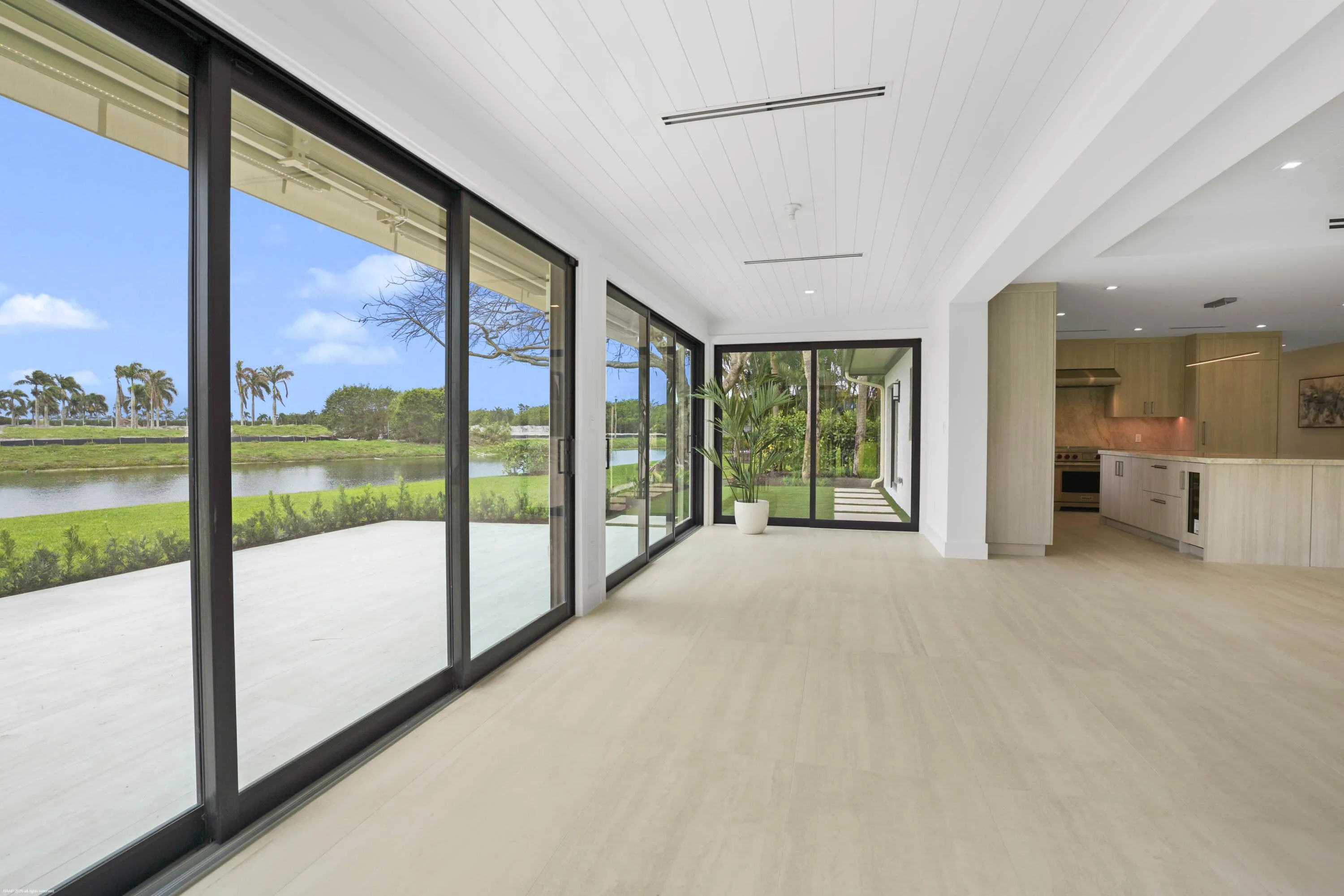 Expansive sliding glass doors, light wood-finish flooring, white shiplap ceiling, recessed lighting, and a neutral color palette