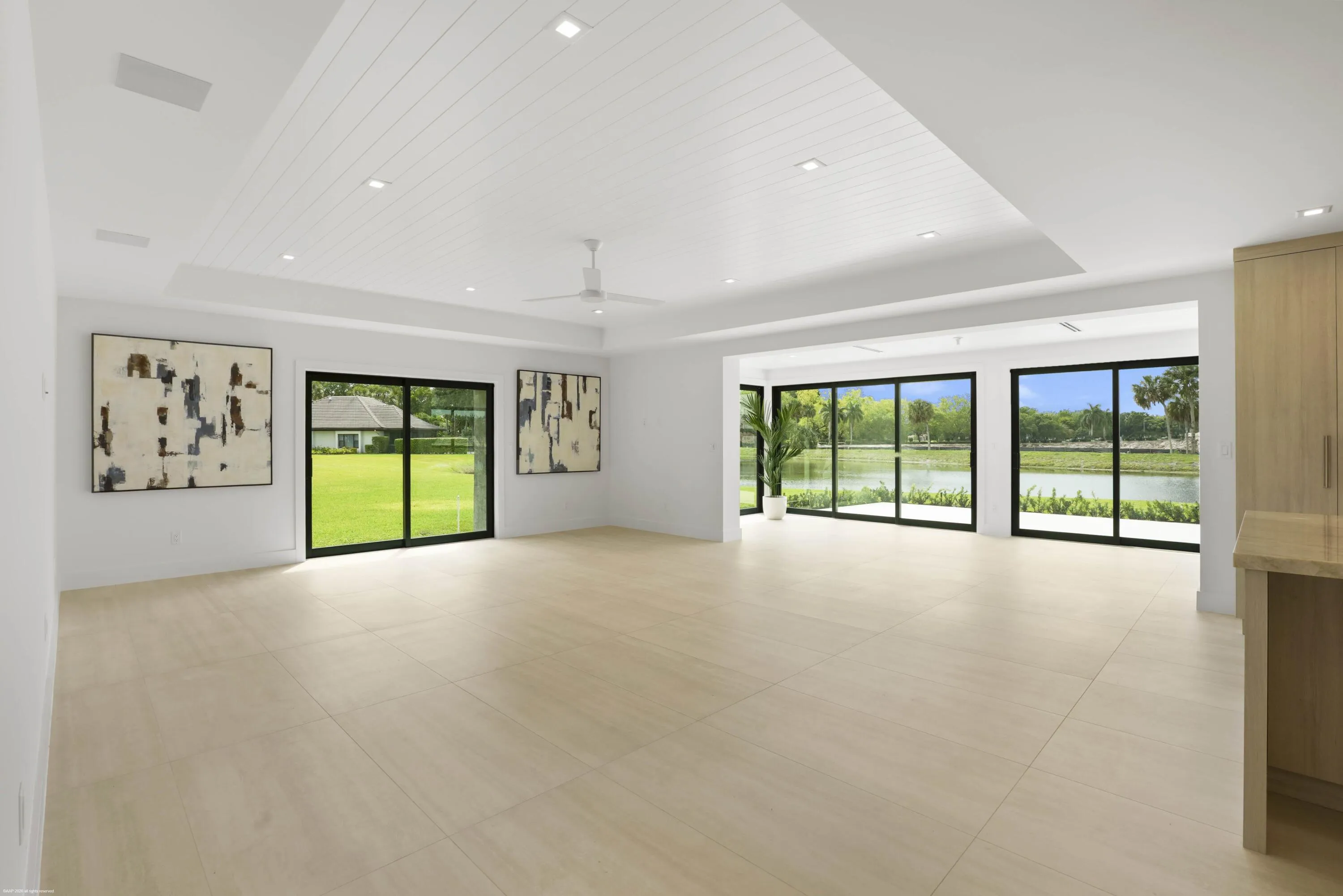 Open-concept living area with large format tile flooring and a tray ceiling featuring recessed lighting