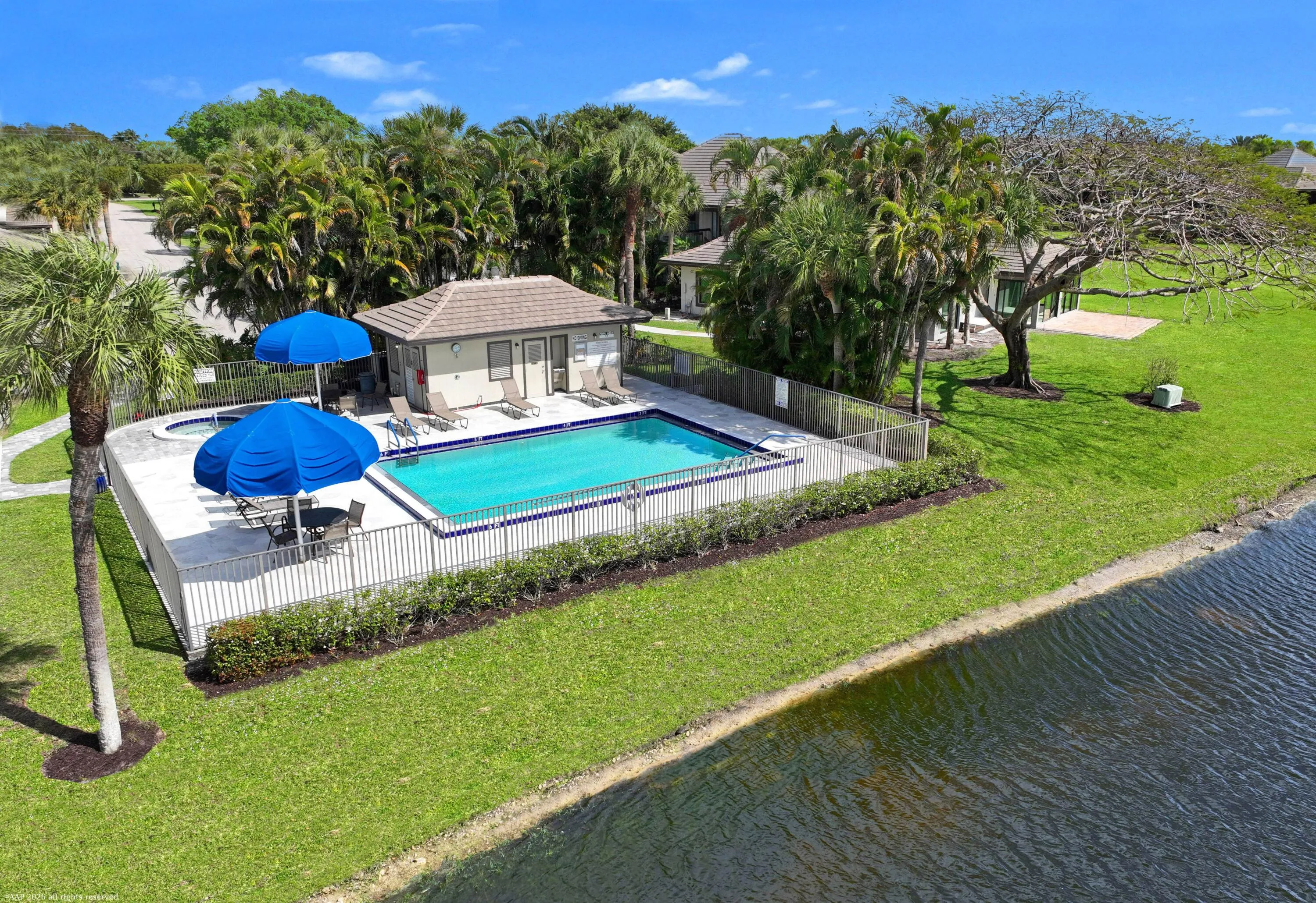 Community swimming pool with surrounding fencing, adjacent spa, and poolside building