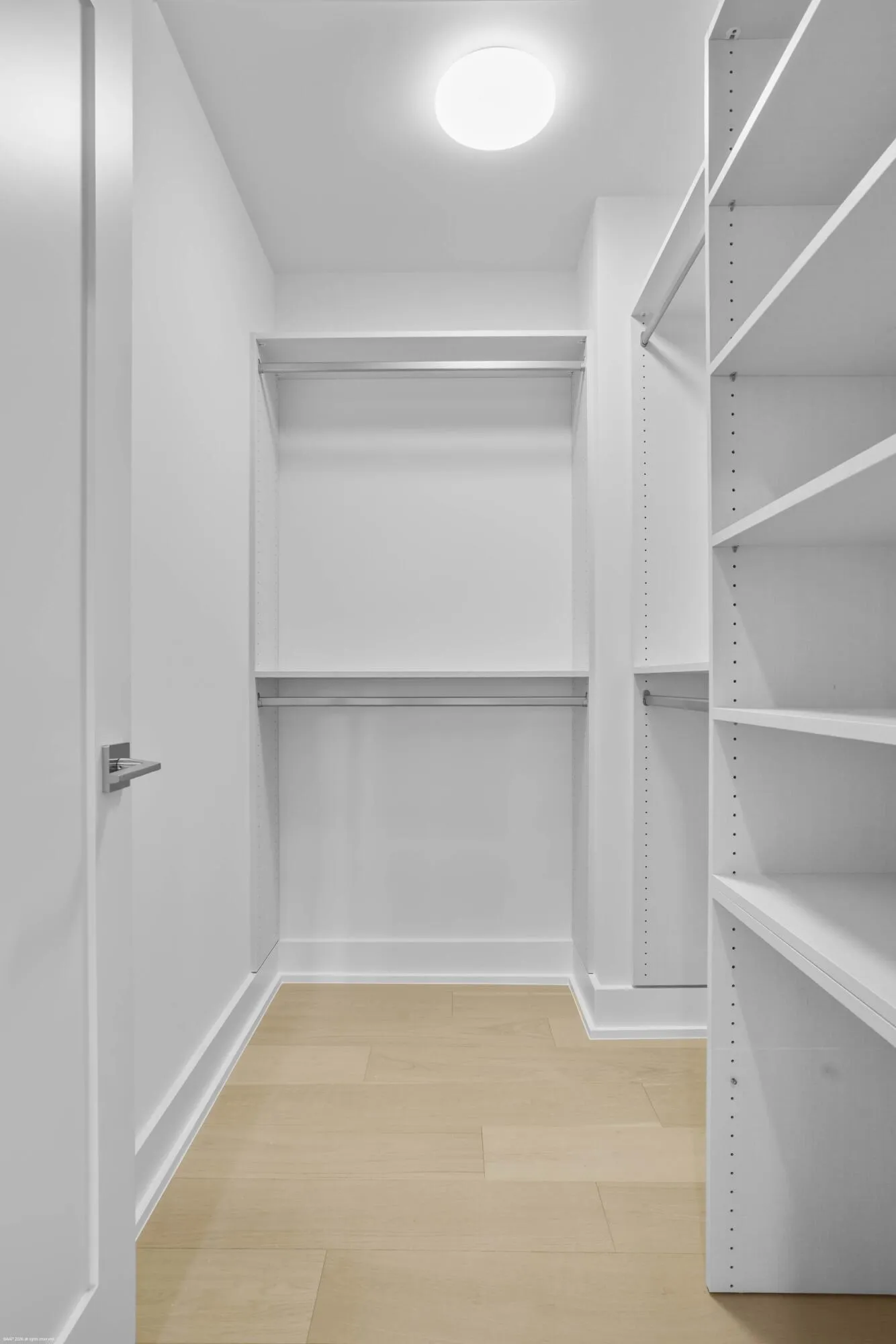 Custom closet system with adjustable shelving, integrated hanging rods, recessed ceiling light, and wood-finish flooring