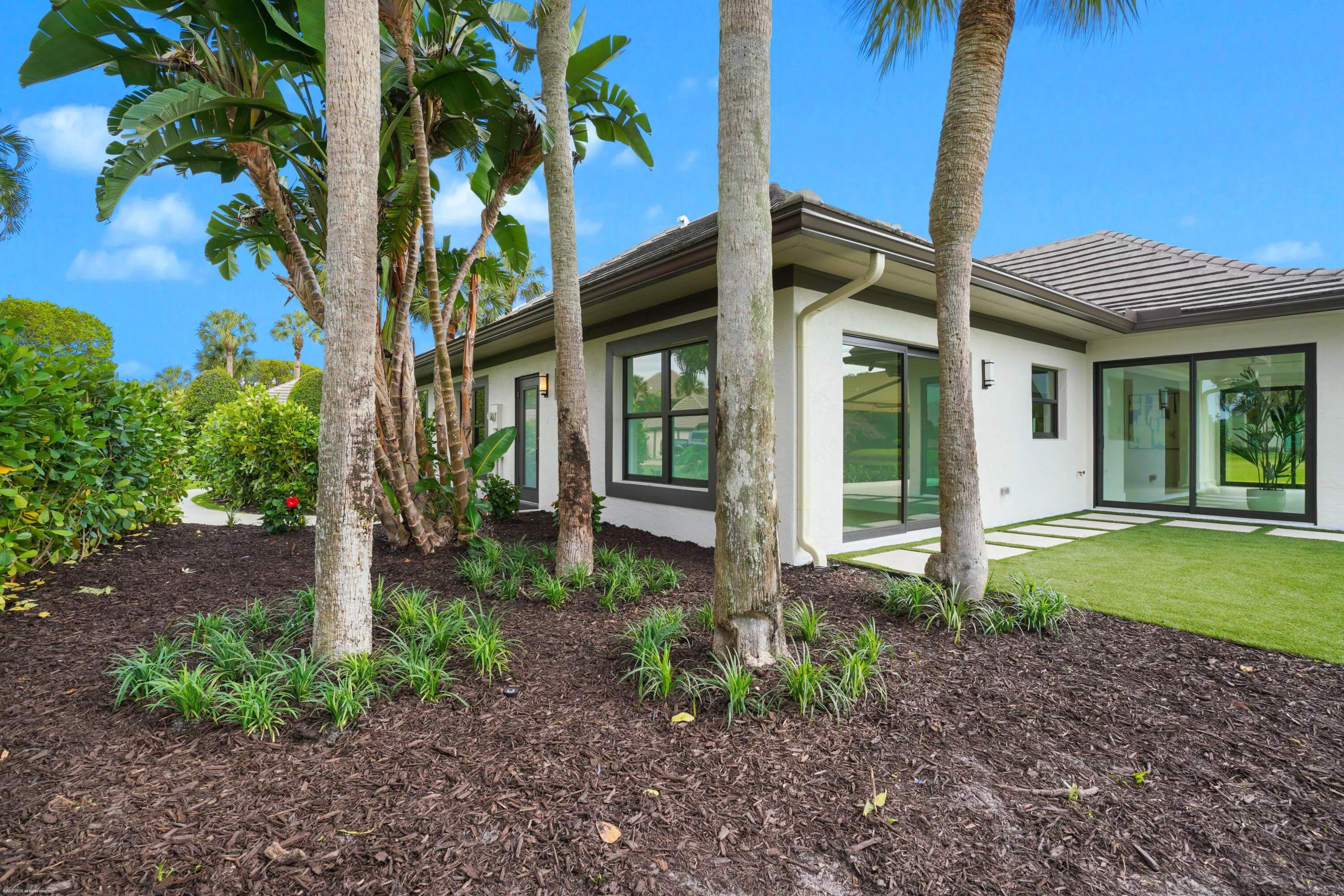 Modern stucco exterior with a tiled roof, large sliding glass doors, and a manicured lawn
