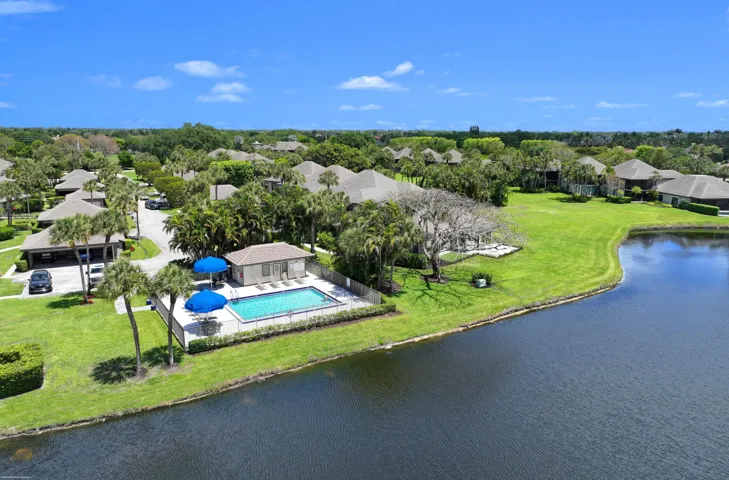 Community pool with a surrounding patio and adjacent building, set among mature landscaping and a body of water