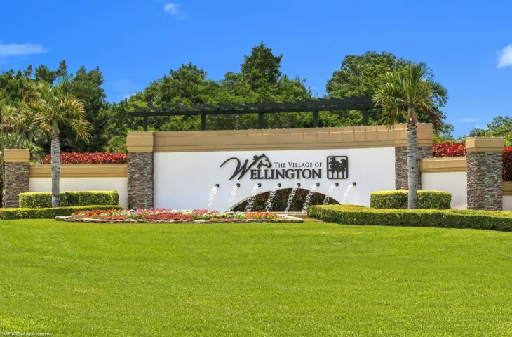 Community entry sign featuring stacked stone columns, a water feature, and integrated landscaping with palm trees