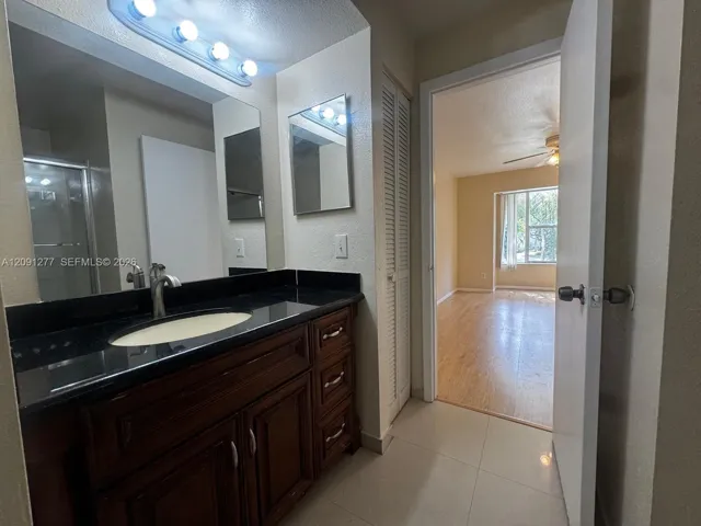 Bathroom featuring a dark-toned stone-surface vanity with an integrated oval sink, wood-finish cabinetry, a large wall-mounted mirror, and tile flooring