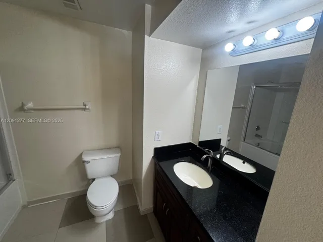 Bathroom featuring a vanity with dark stone countertop, undermount oval sink, dark wood-finish cabinetry, and three-bulb vanity light fixture