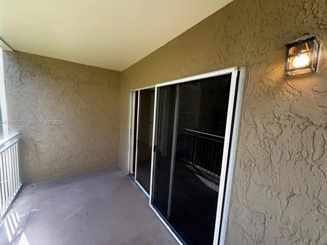 Covered balcony featuring textured stucco walls, sliding glass door, white metal railing, and an attached wall-mounted lantern light fixture