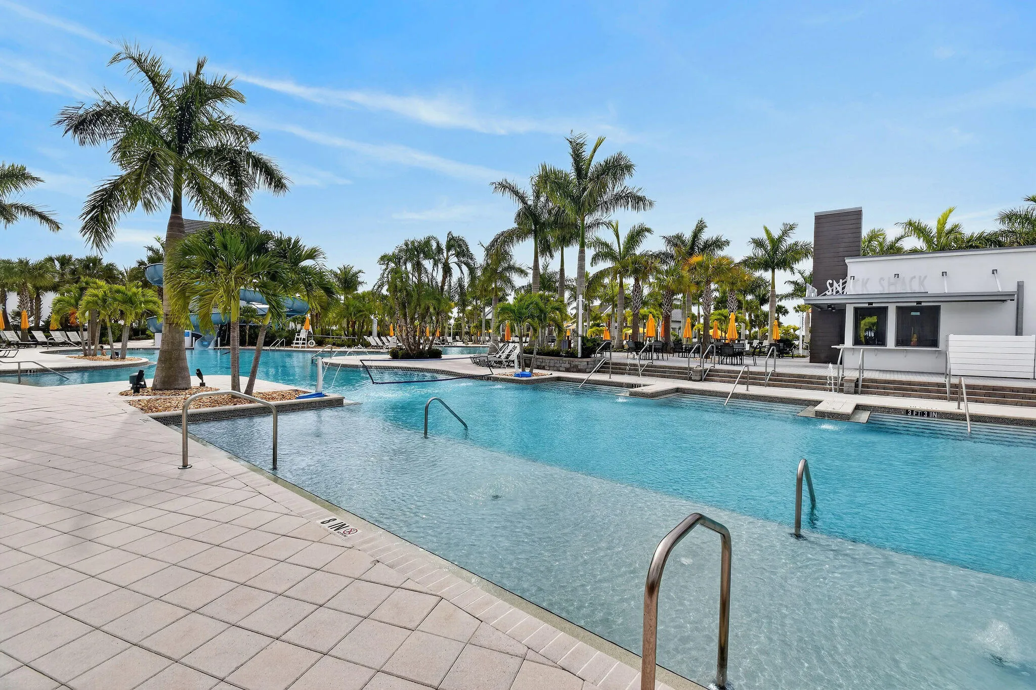 Expansive outdoor pool area featuring multiple swimming zones, integrated water features, surrounding palm trees, and a tiled pool deck