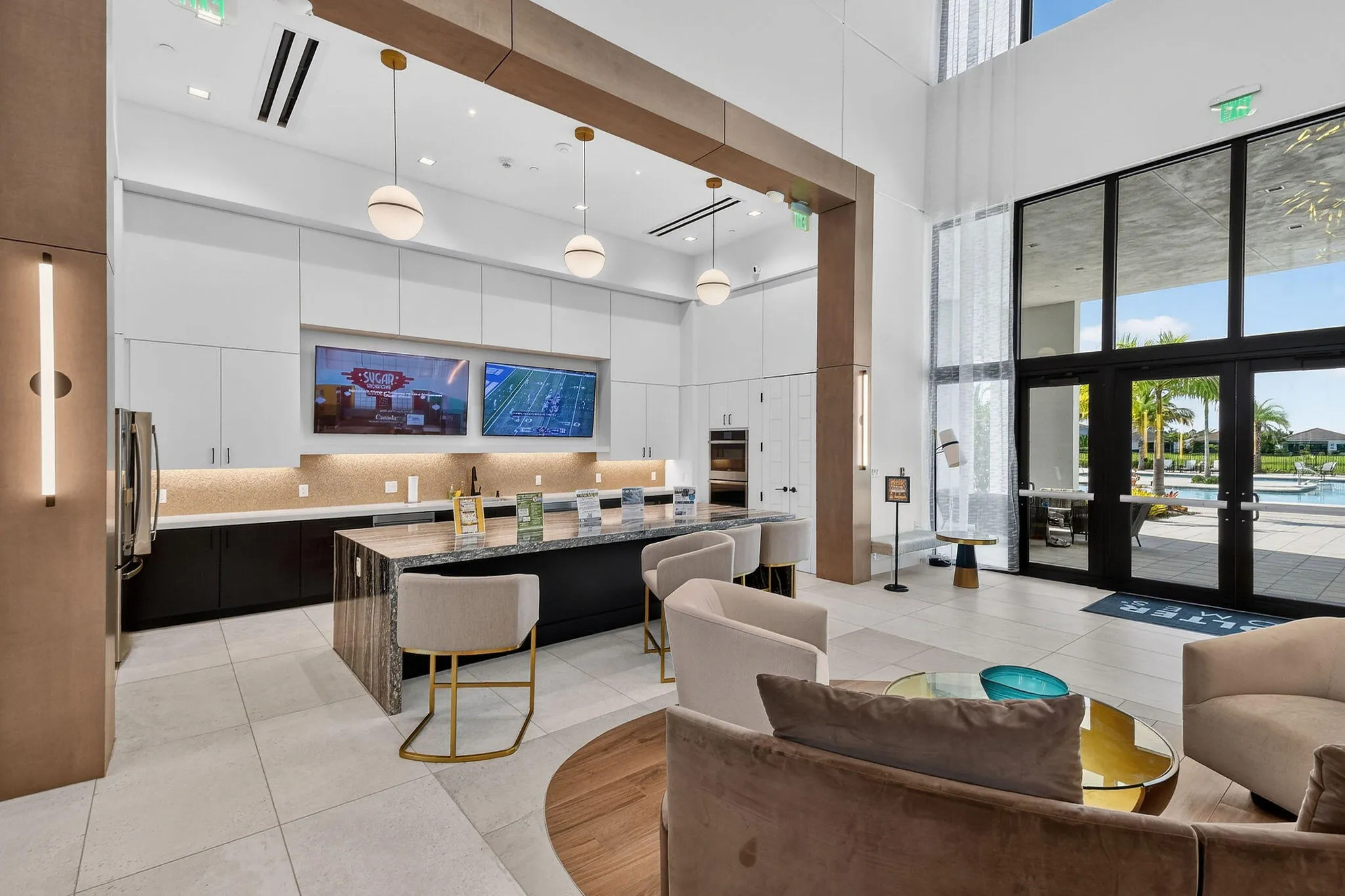 Spacious common area featuring an expansive counter with integrated seating, dual wall-mounted displays, and floor-to-ceiling windows