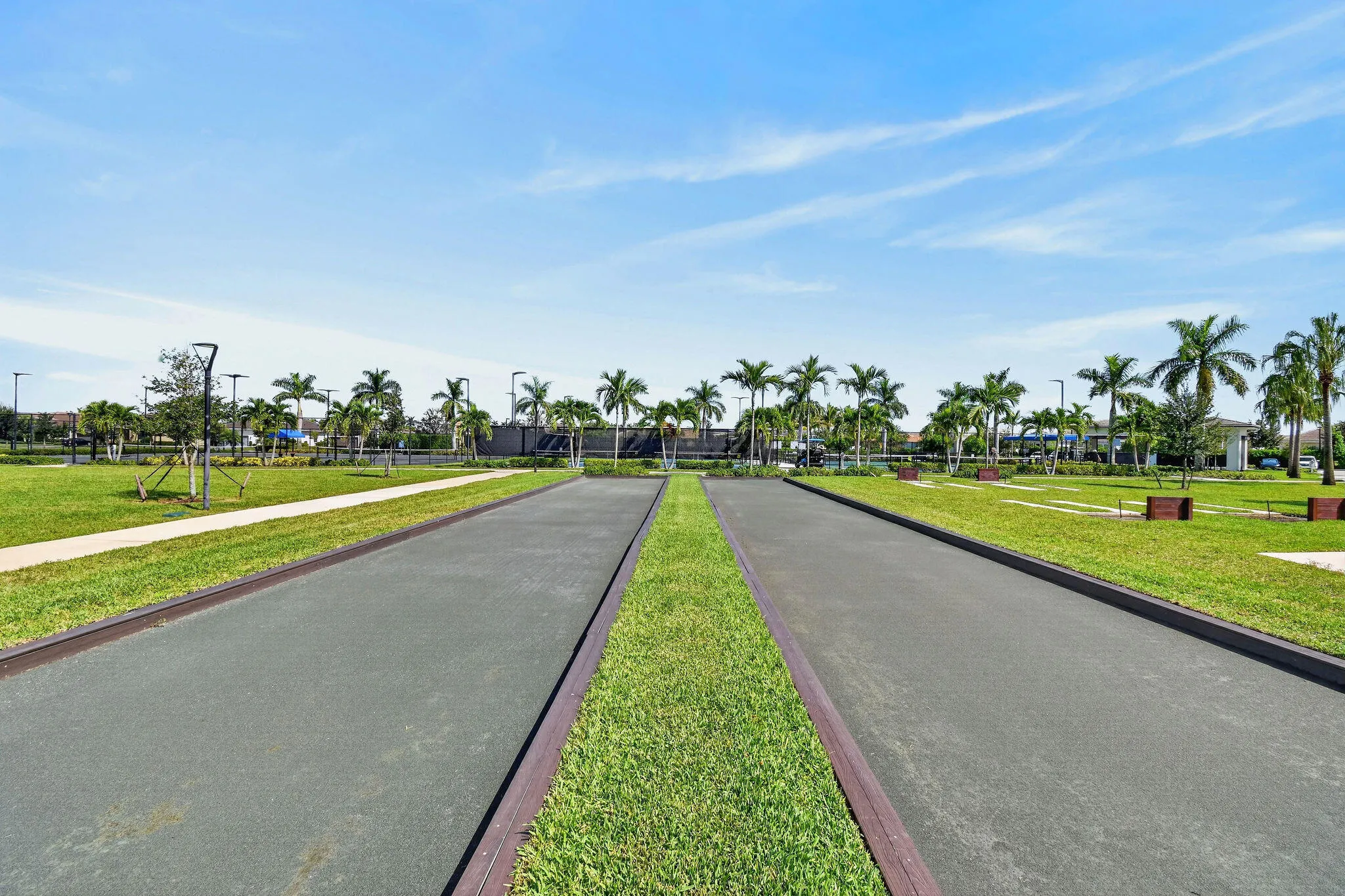 Bocce ball court with dark gray surfacing, bordered by green grass and concrete pathways
