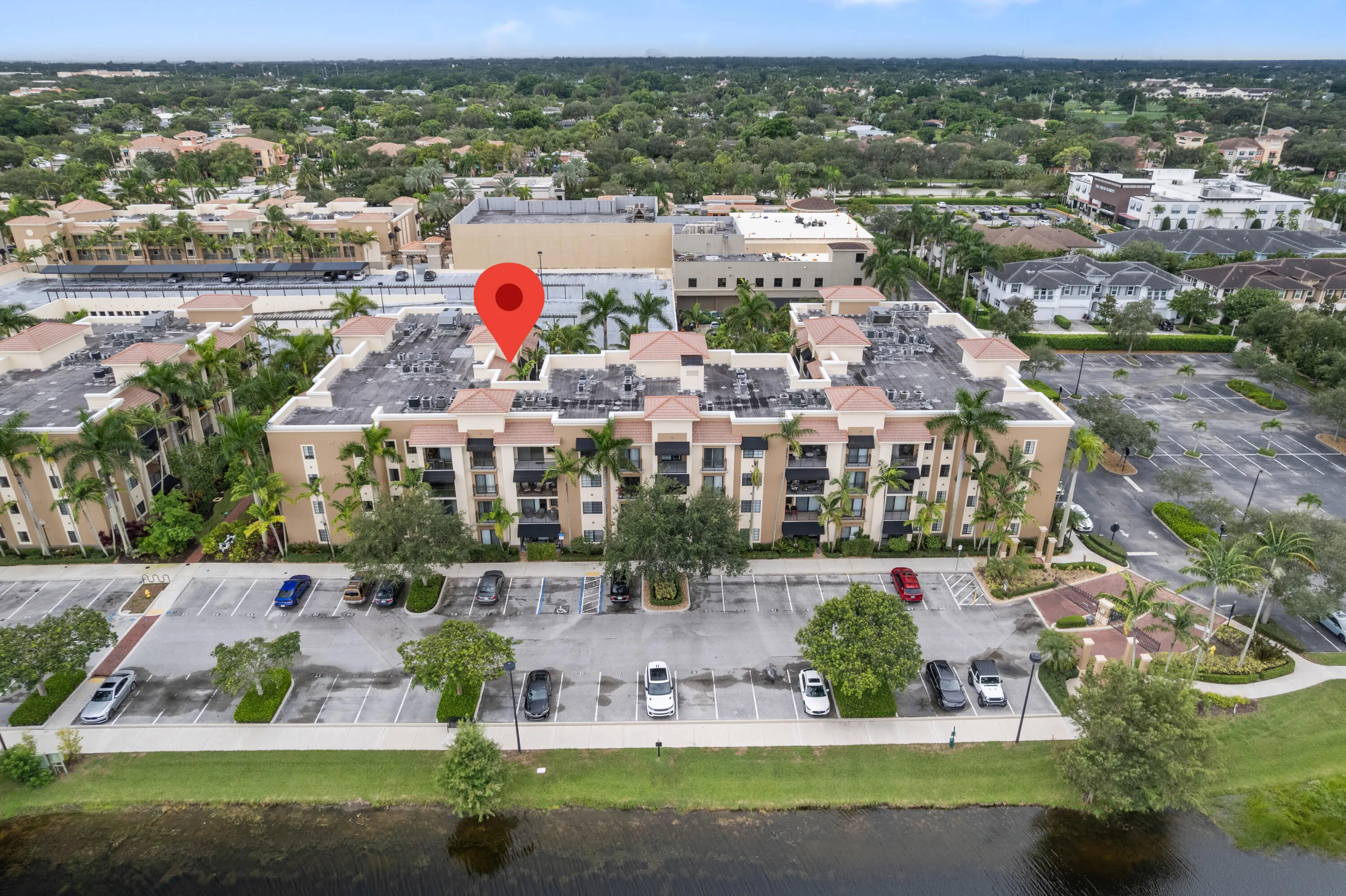 Multi-story residential building with balconies, surrounding parking areas, and mature palm trees