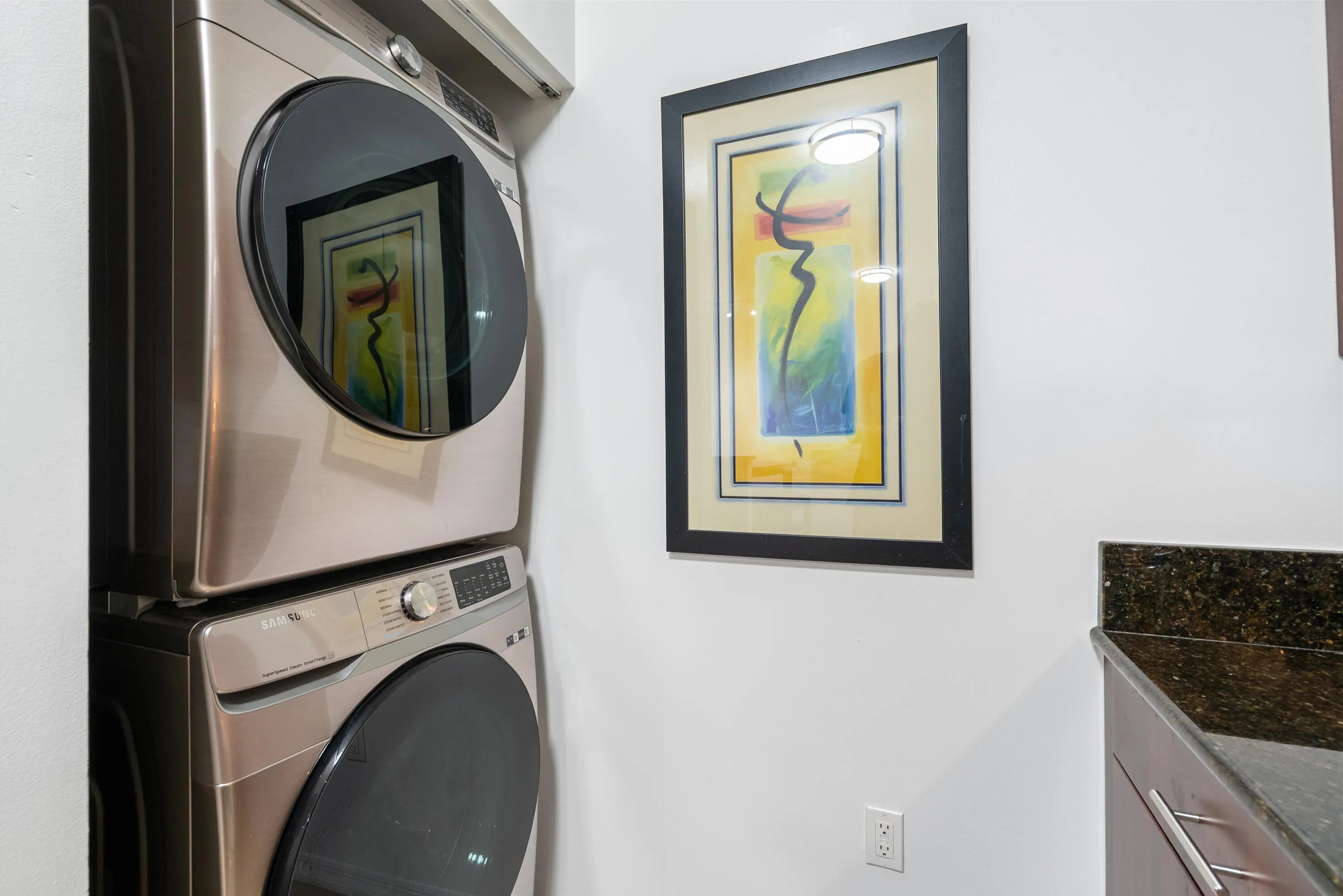 Stacked laundry appliances and a counter with a dark stone-finish surface