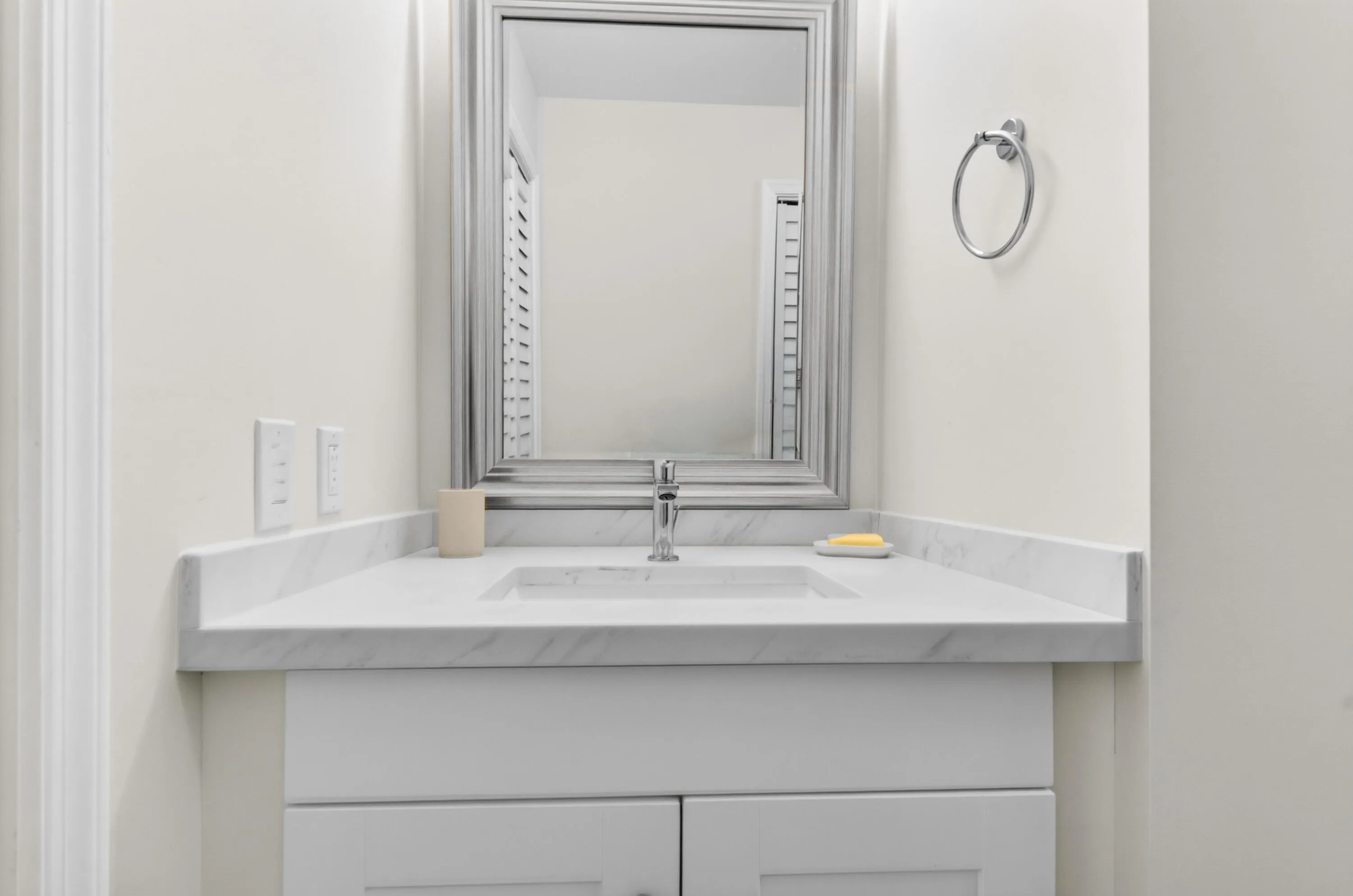 White vanity with a polished chrome faucet, under-mount sink, and a framed mirror